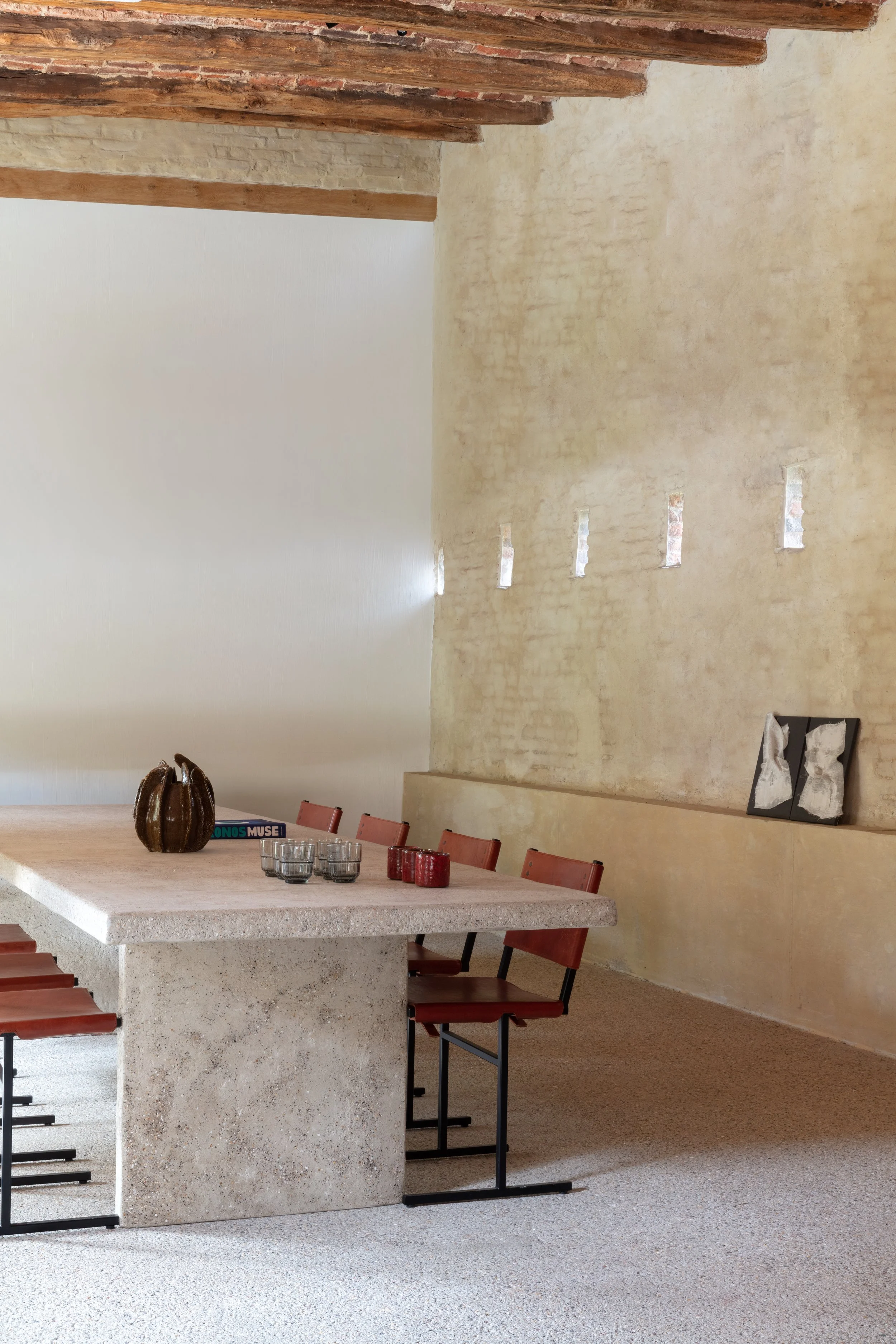 Moderne eetruimte met grote natuurstenen tafel, rode stoelen en een beige structuurwand.