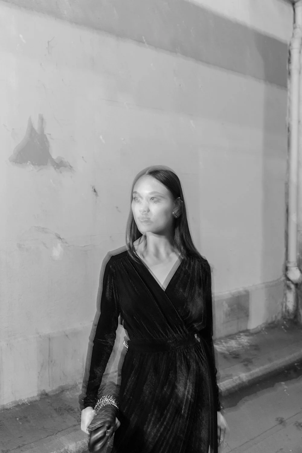 Elegant zwart-witmodebeeld van een vrouw in een donkere jurk in een stedelijke omgeving.