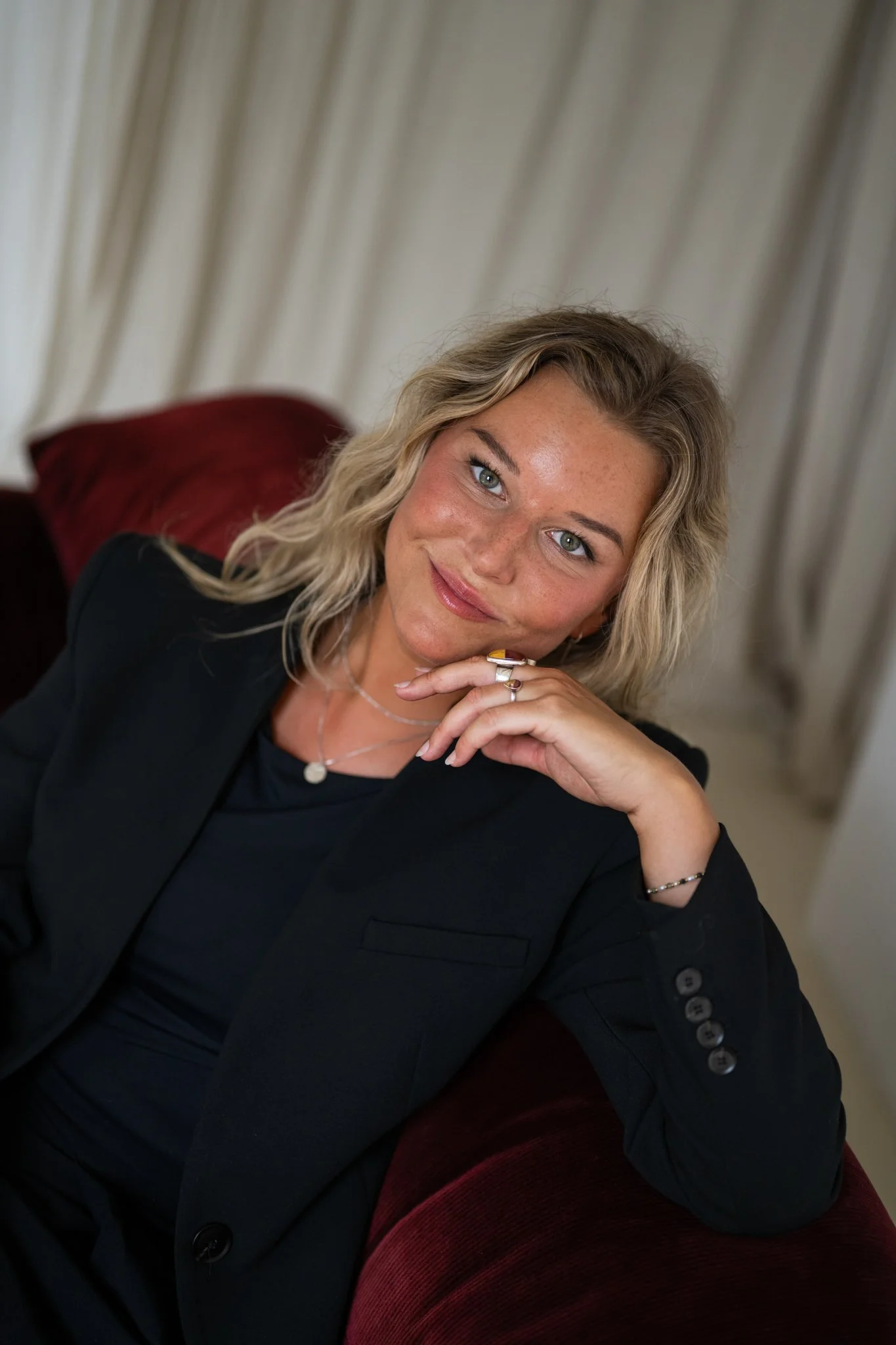 Persoonlijk portret van Céline Ronsse van Studio Cé in een zwarte blazer, zittend in een rode fluwelen zetel.
