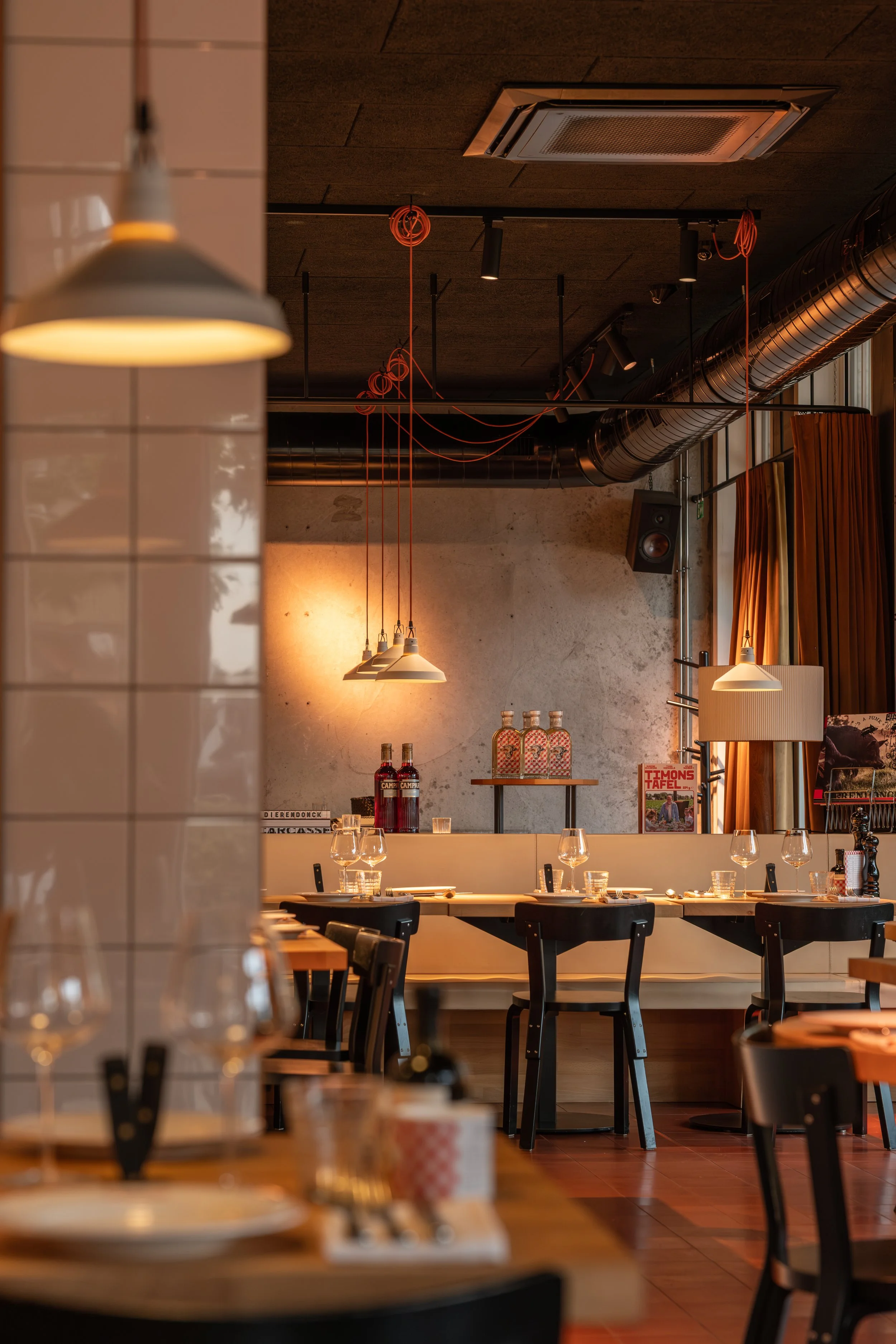Sfeervol restaurantinterieur met gedekte tafels, zwarte stoelen en warme hangverlichting.