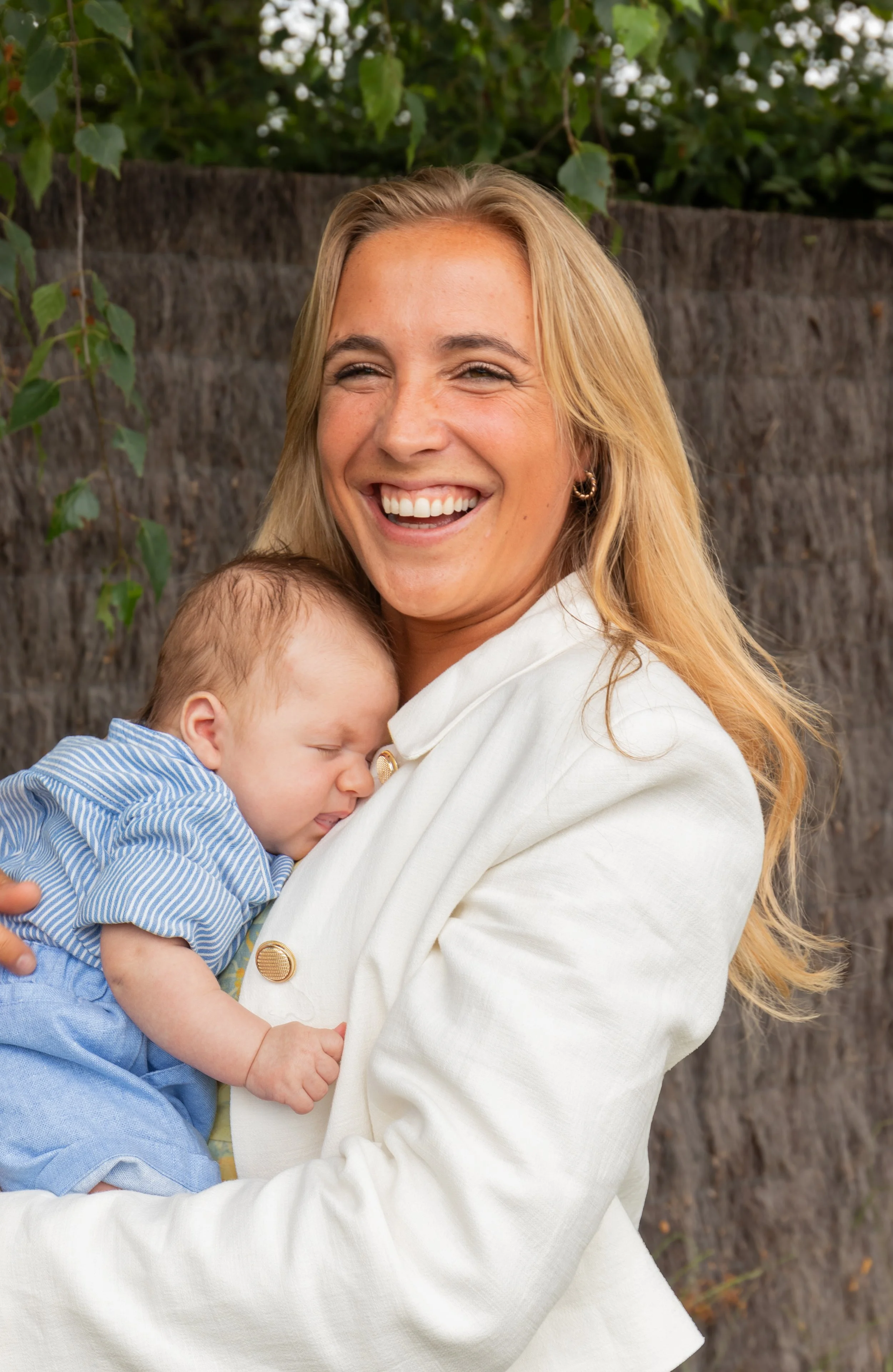 Lachende vrouw houdt een slapend kindje vast tijdens een familiefeest.