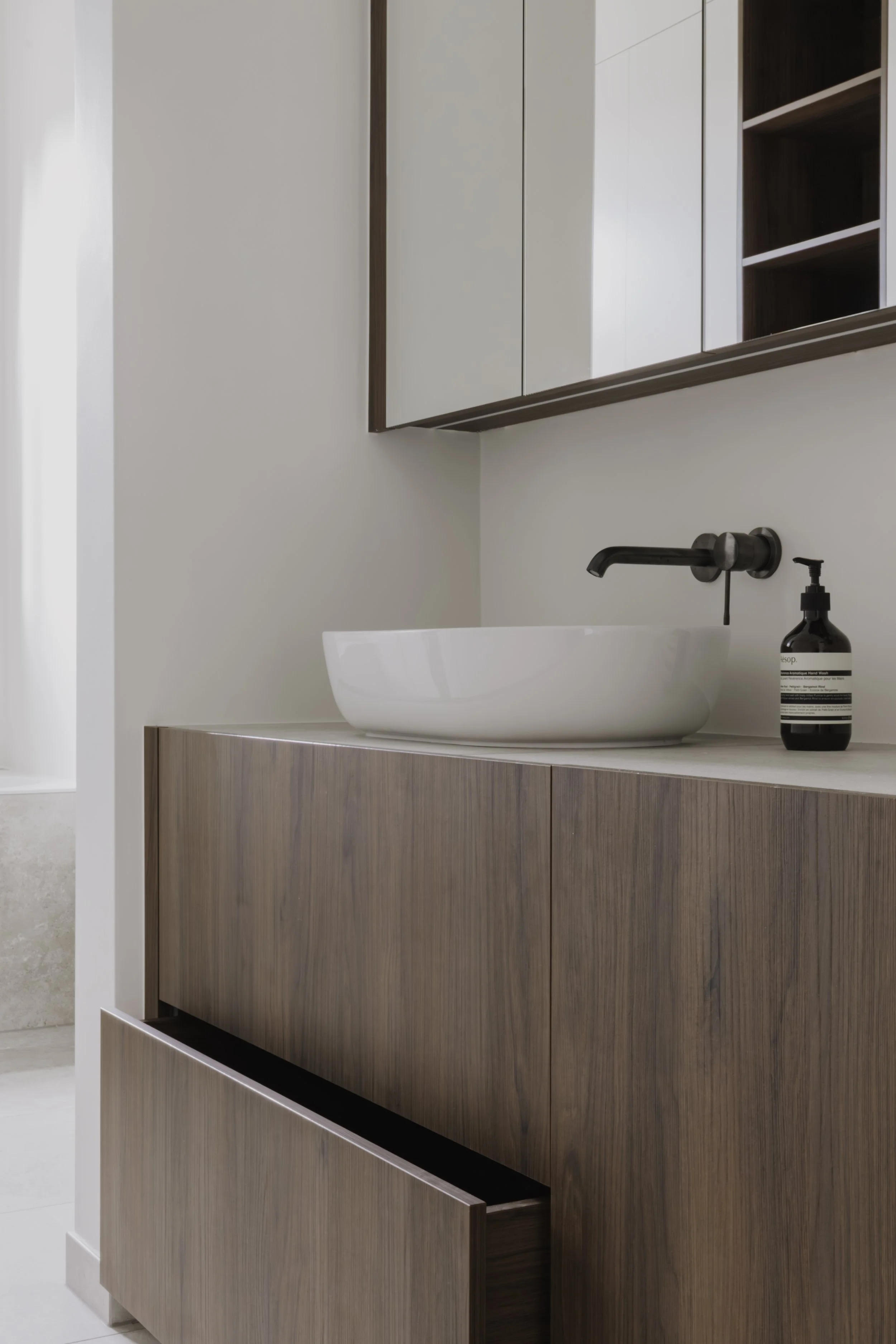 Interieurdetail van een moderne badkamer met witte waskom, wandkraan en houten maatkast.