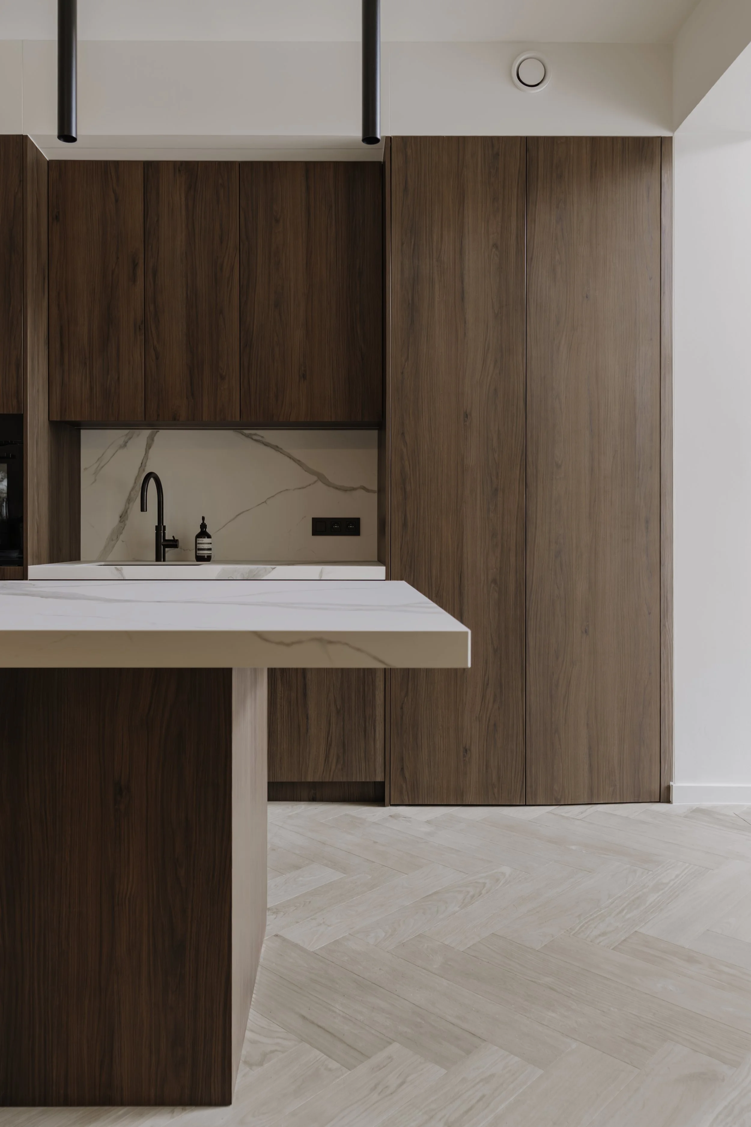 Professionele interieurfotografie van een moderne keuken met houten kasten, marmeren spatwand en zwarte kraan.