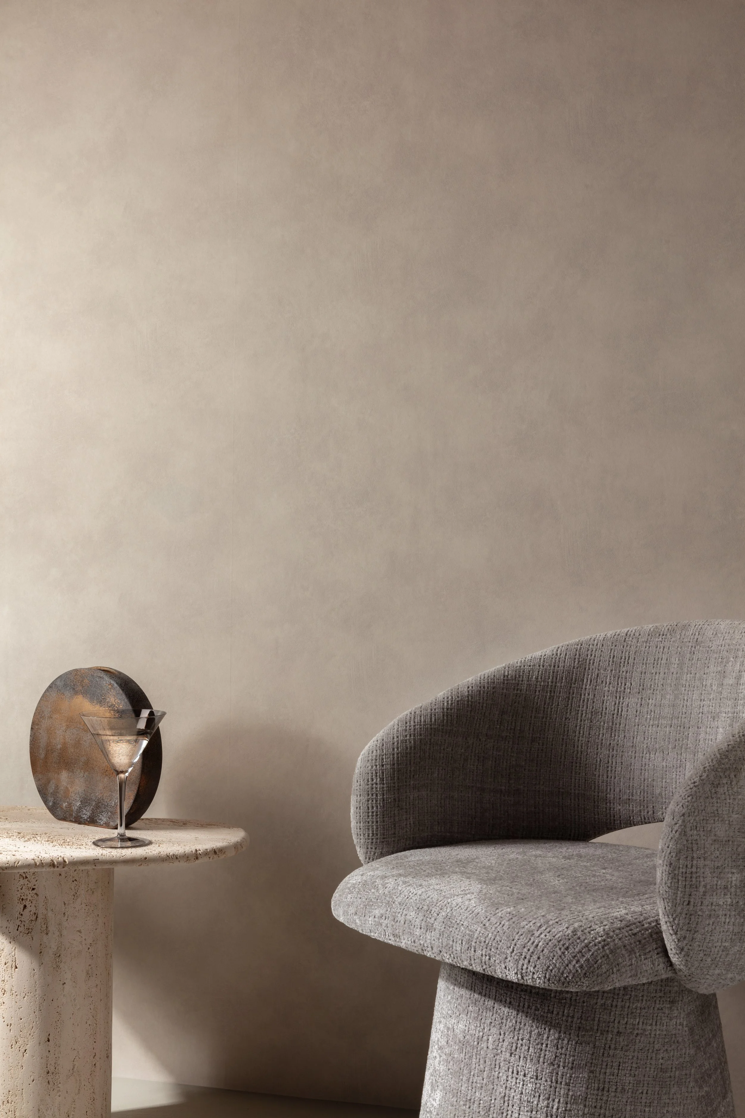 Sfeervol interieurdetail met een beige fauteuil, ronde bijzettafel en decoratieve wandkunst.