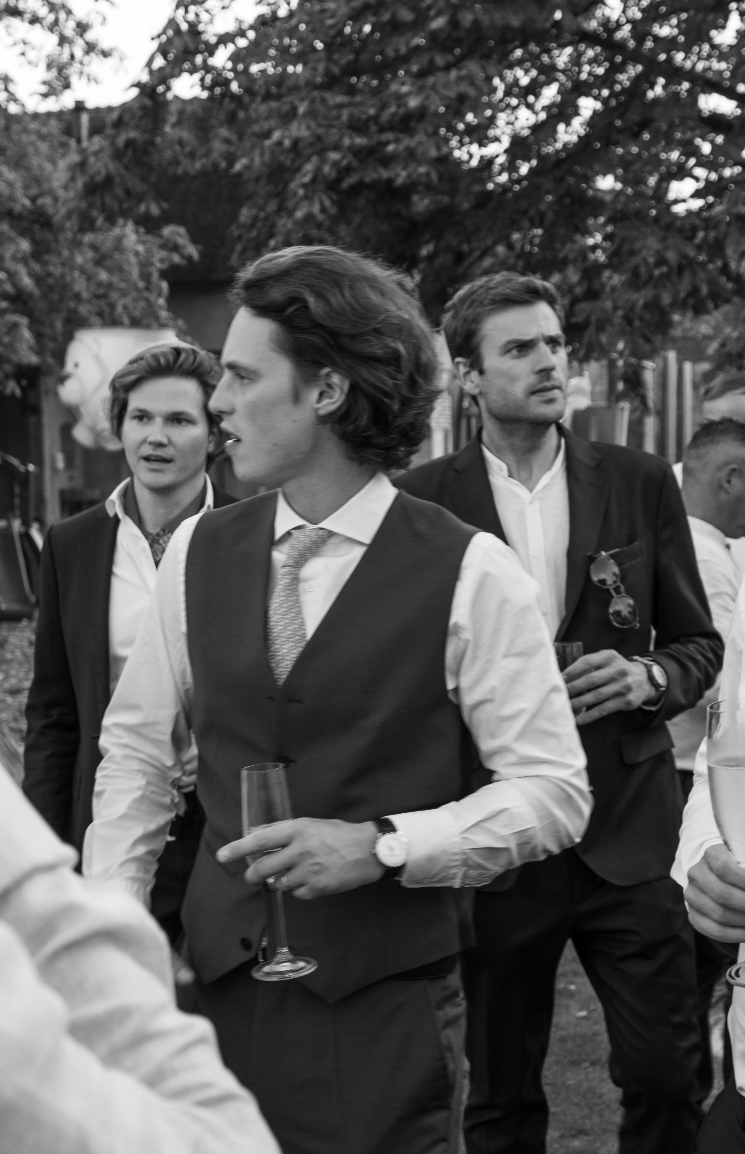Zwart-witfoto van stijlvol geklede mannen met champagne tijdens een familiefeest.