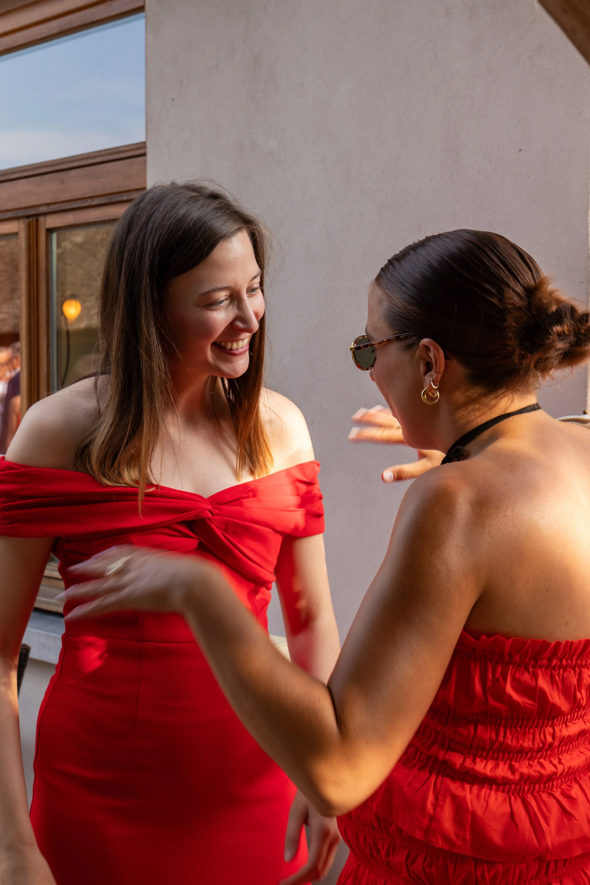 Twee vrouwen in rode jurken lachen samen tijdens een buitenevenement.