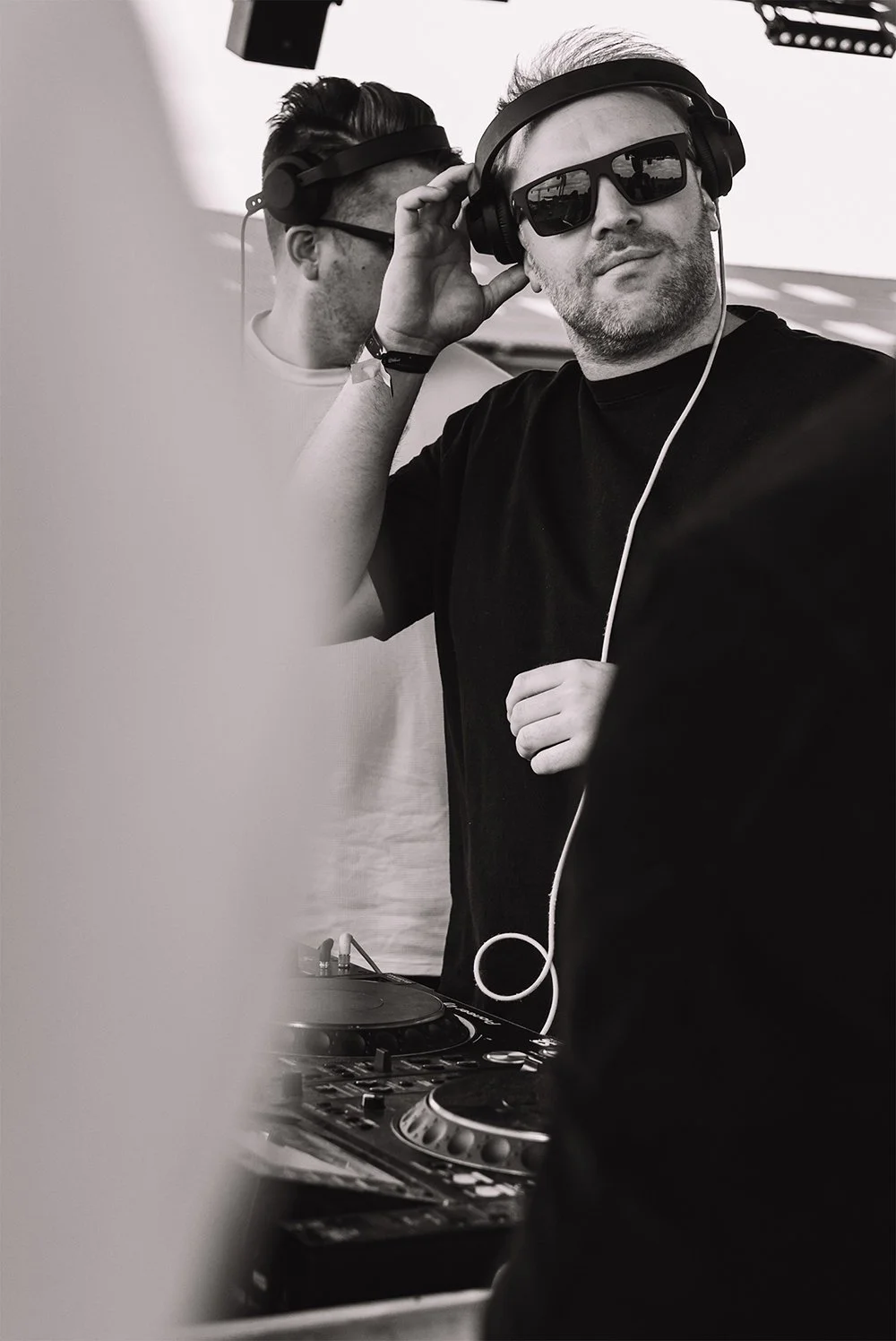 Spontaan zwart-witportret van een dj met zonnebril en hoofdtelefoon achter zijn draaitafel.