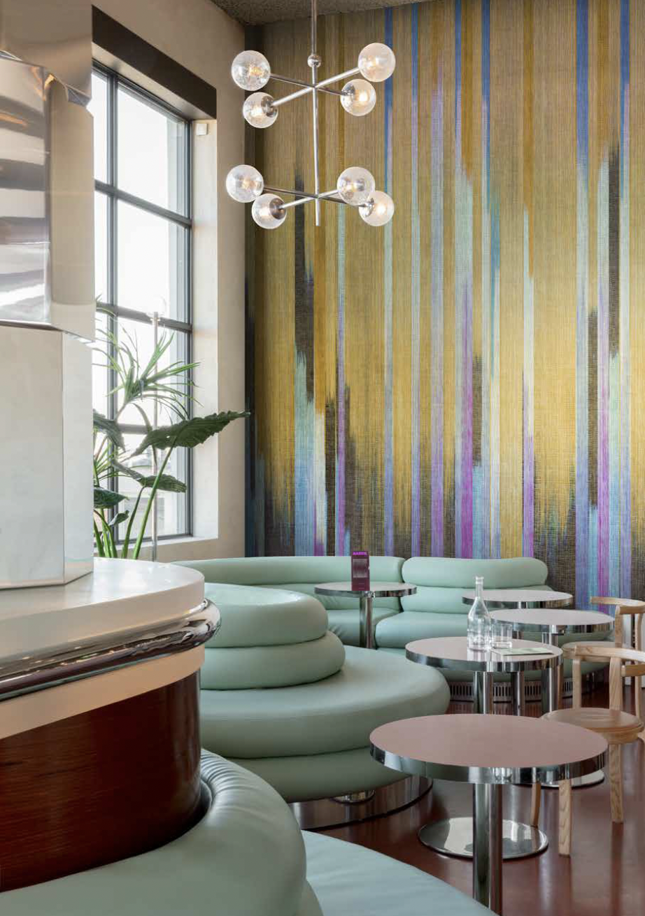 Interieurfotografie van een moderne horecazaak met mintgroene zitbanken, kleurrijke wand en opvallende verlichting.