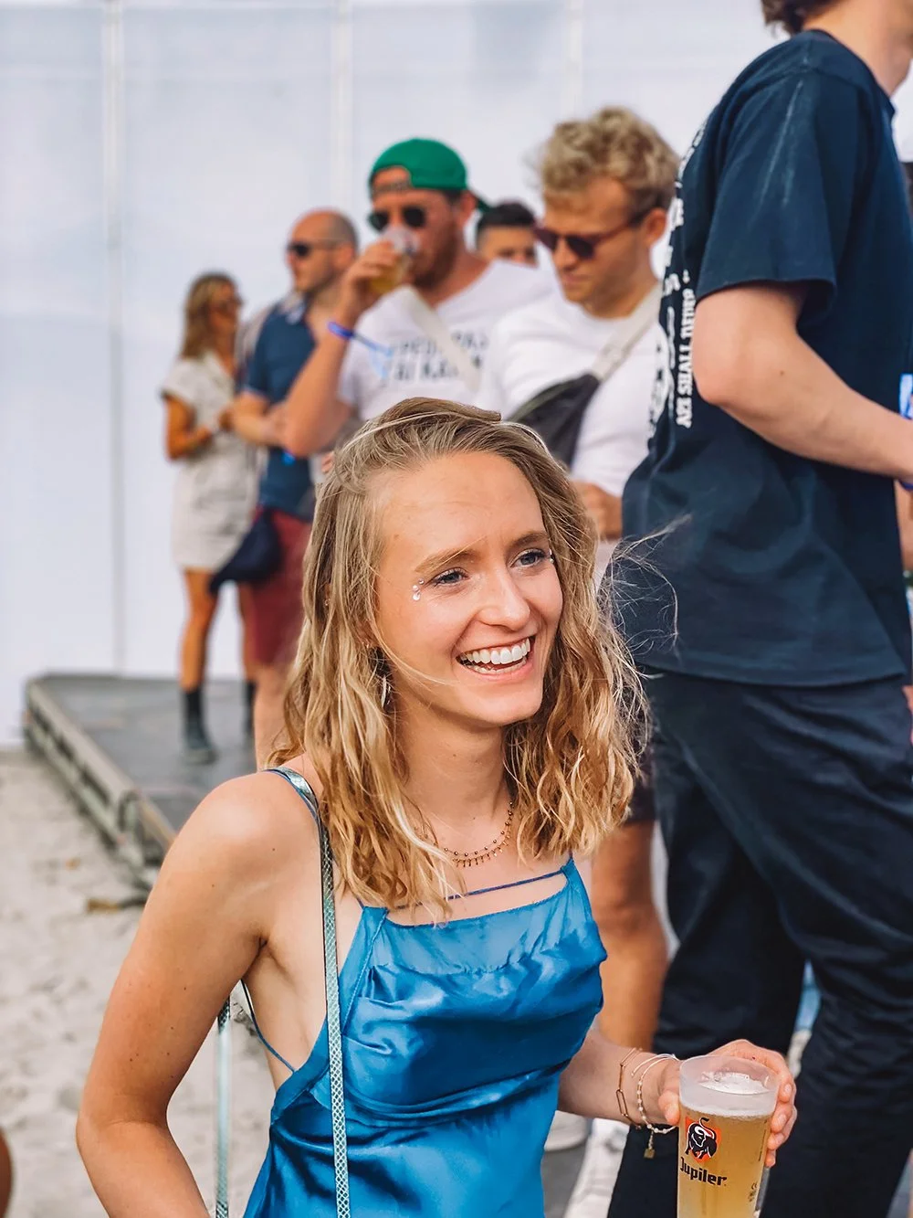 Lachende vrouw in een blauwe jurk met een drankje tijdens een feest in openlucht.