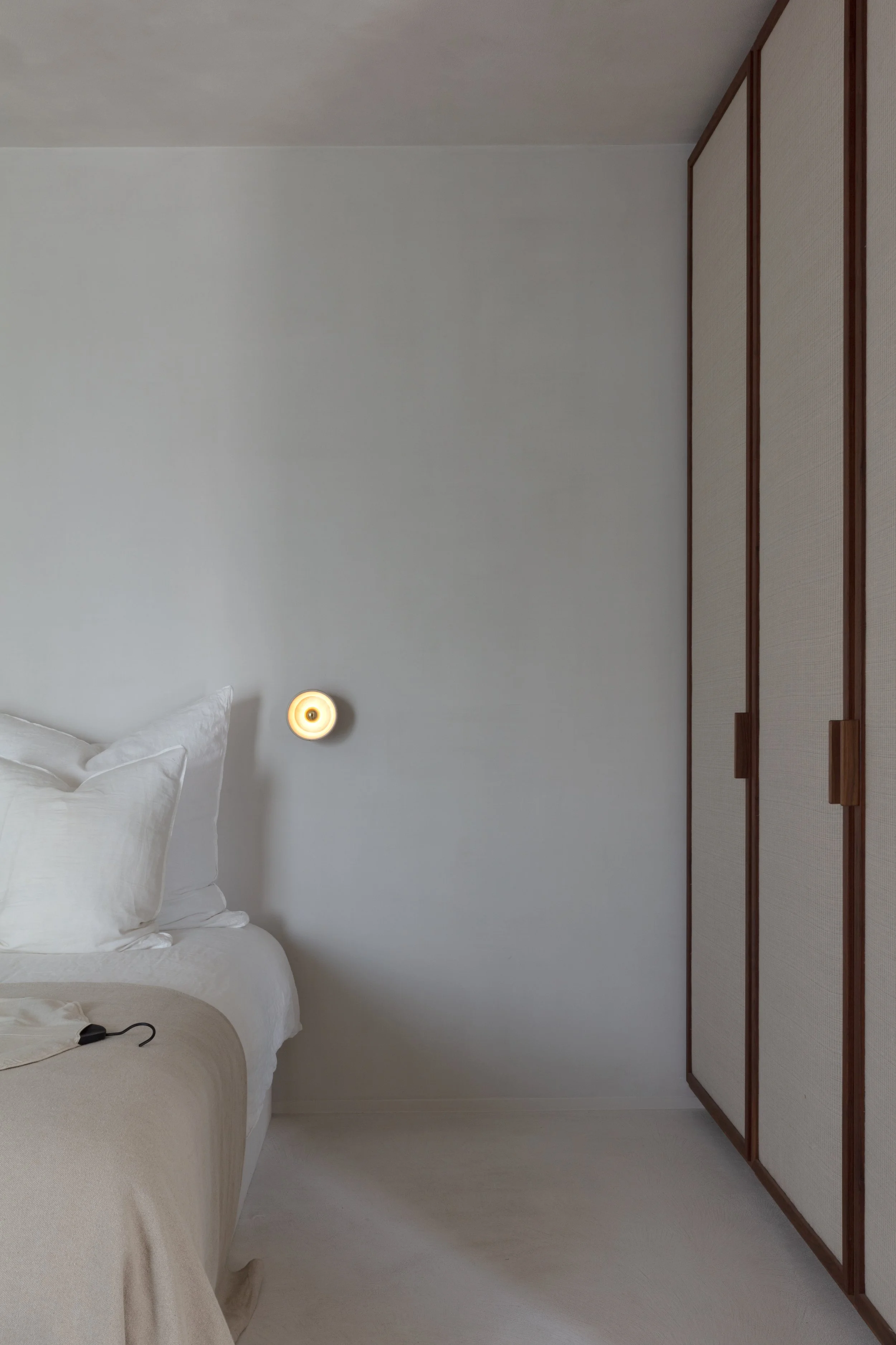 Minimalistische slaapkamer met beige bed, ingebouwde kast en sfeervolle wandverlichting.