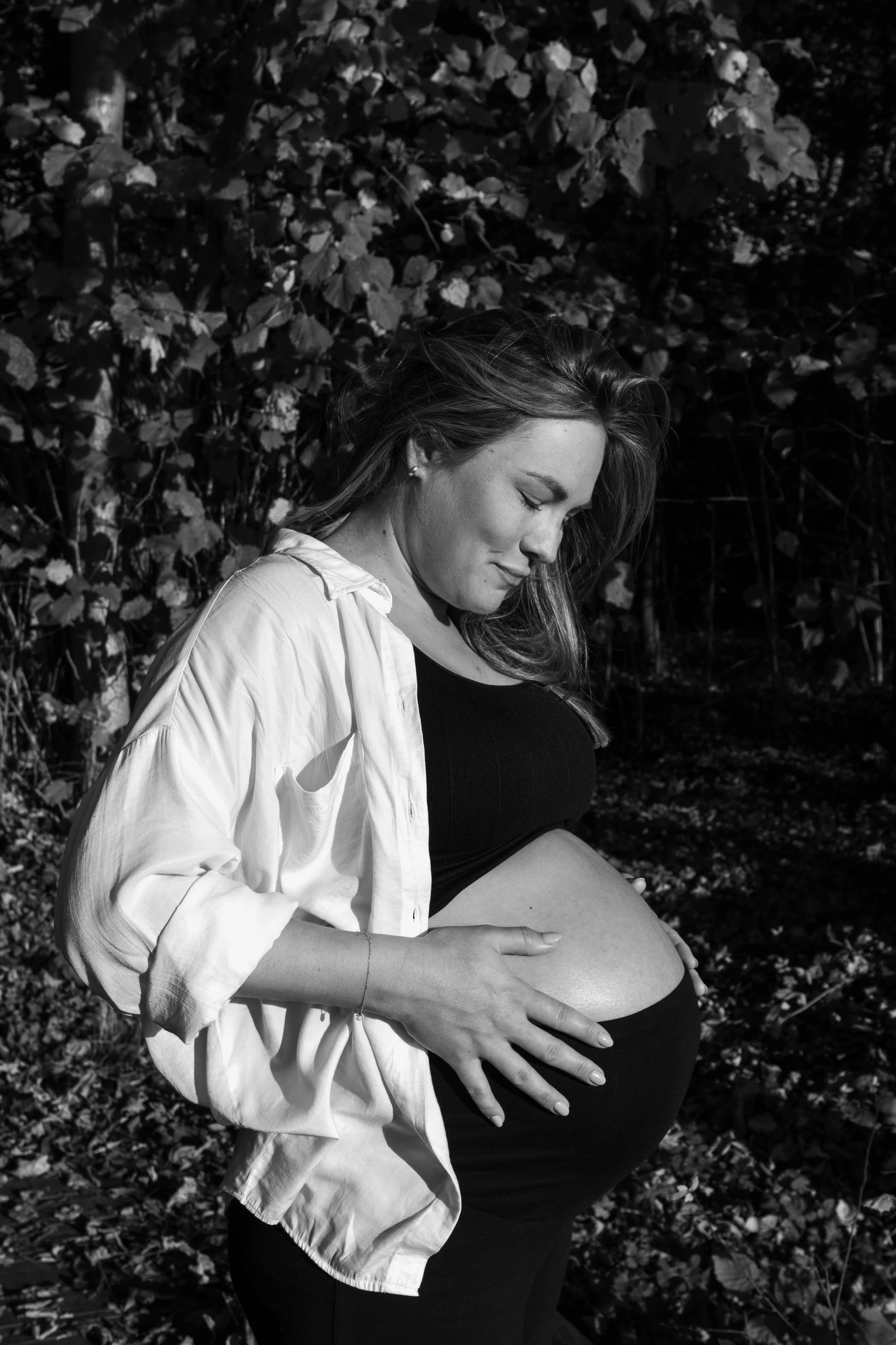 Tijdloos zwart-wit zwangerschapsportret van een aanstaande mama in een groene buitenomgeving.