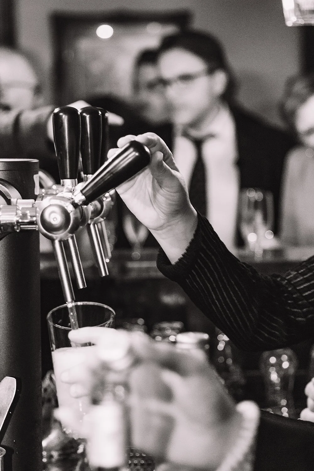 Zwart-wit detail van een bartender die een glas bier tapt aan de bar.