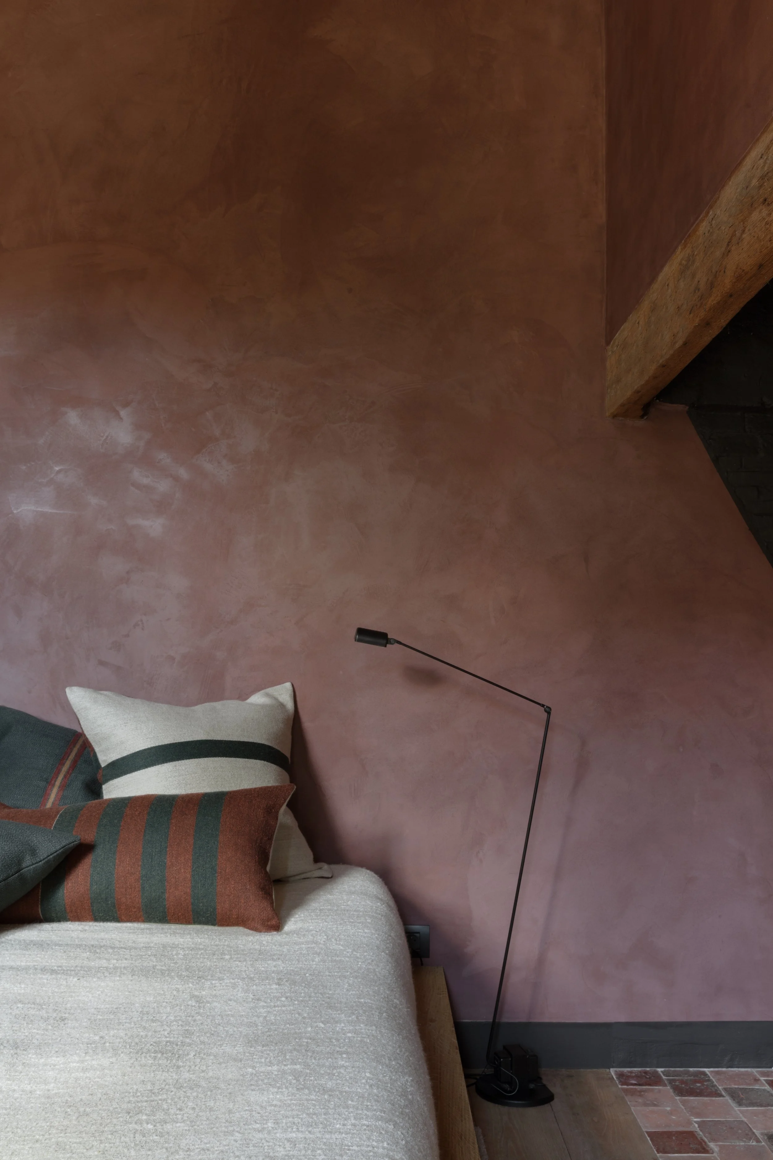 Sfeervolle slaapkamer met roze structuurwand, houten hoofdbord en decoratieve kussens.