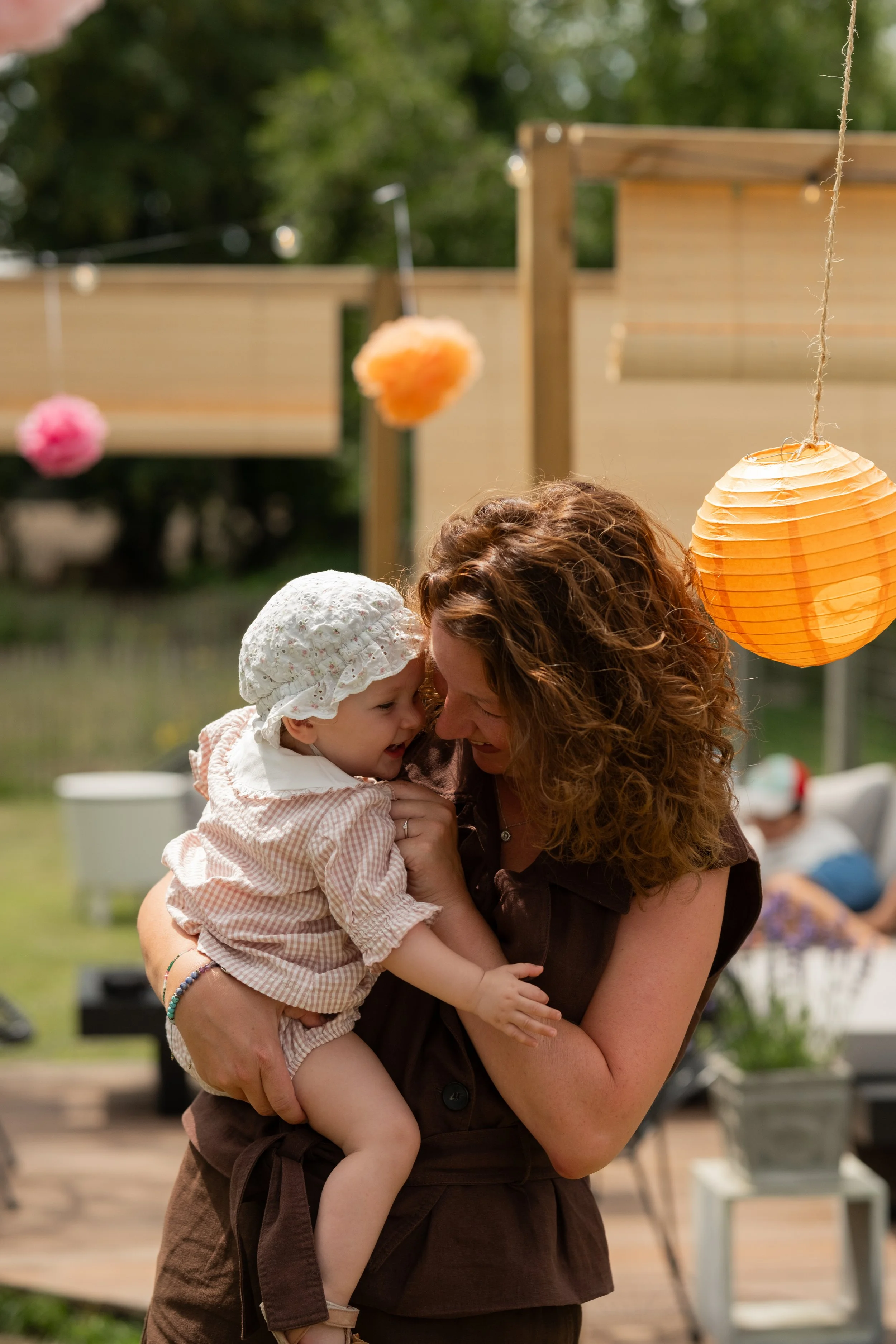 Moeder houdt haar dochtertje liefdevol vast tijdens een familiefeest met kleurrijke lampionnen.