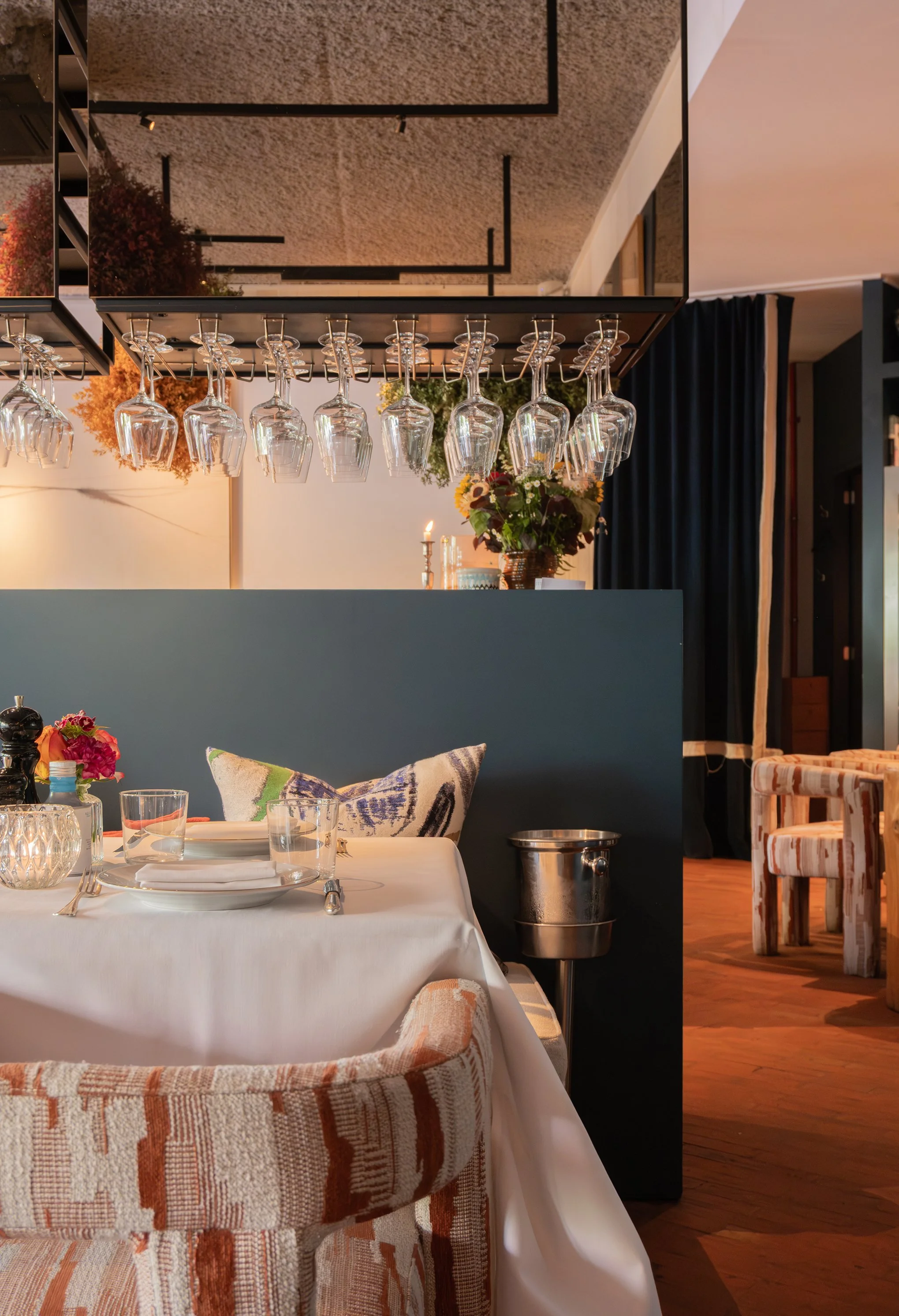 Sfeervol restaurantinterieur met gedekte tafels, bloemen en hangende wijnglazen.