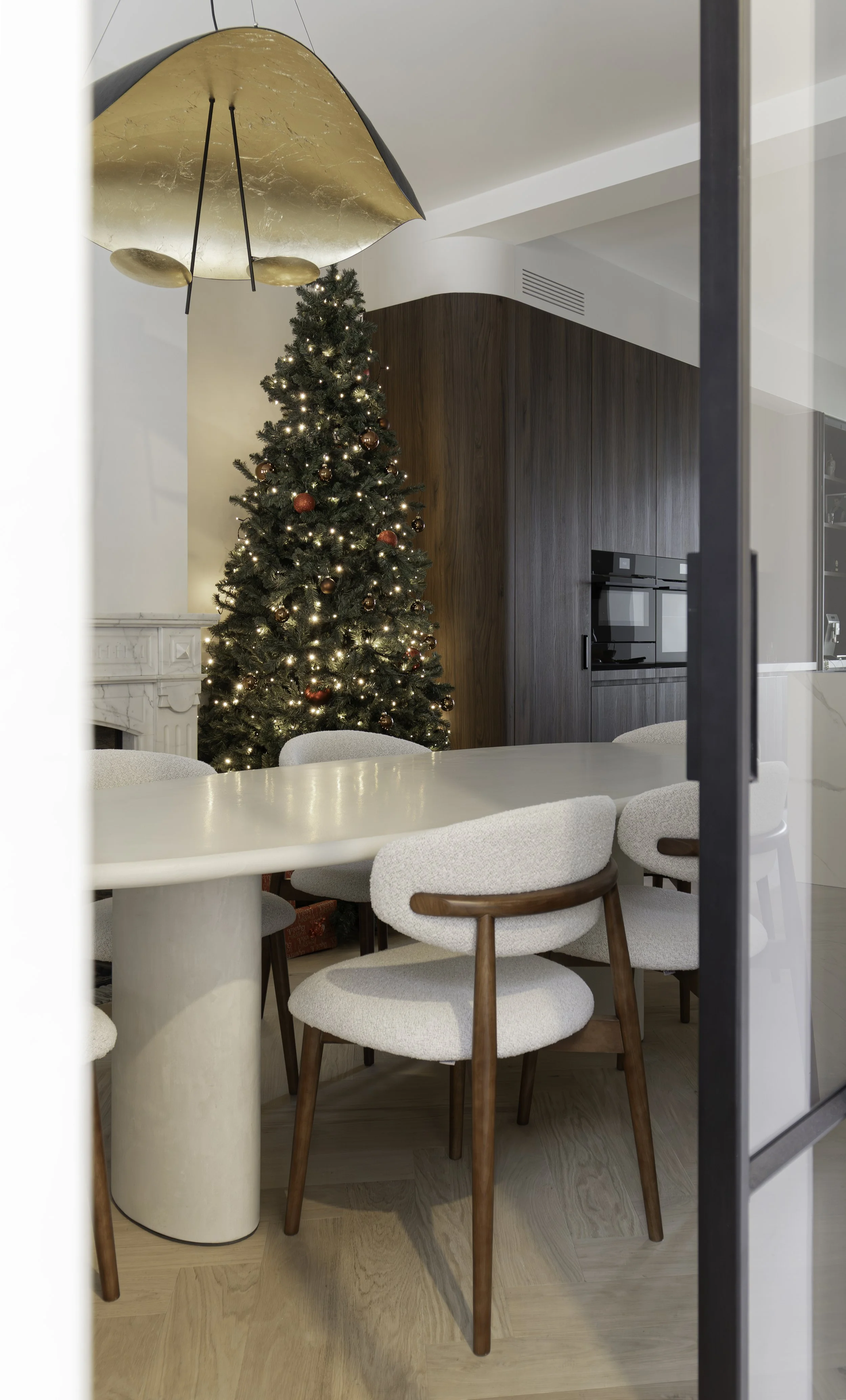 Moderne eetruimte met witte tafel en stoelen en een sfeervol versierde kerstboom.