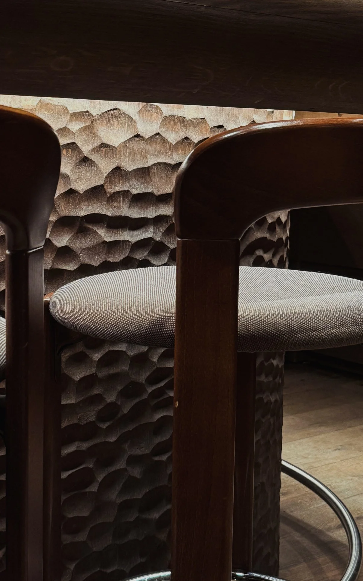 Sfeervol interieurdetail van een houten tafel, gestoffeerde stoelen en een wand met honingraatstructuur.