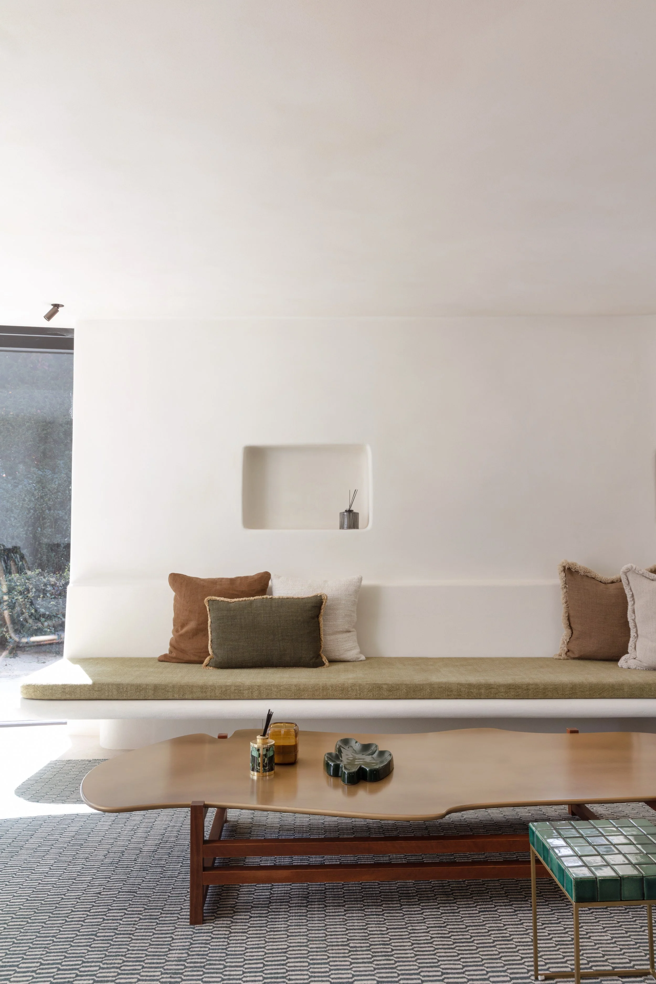 Minimalistische woonkamer met ingebouwde zitbank, zachte kussens en houten salontafel.