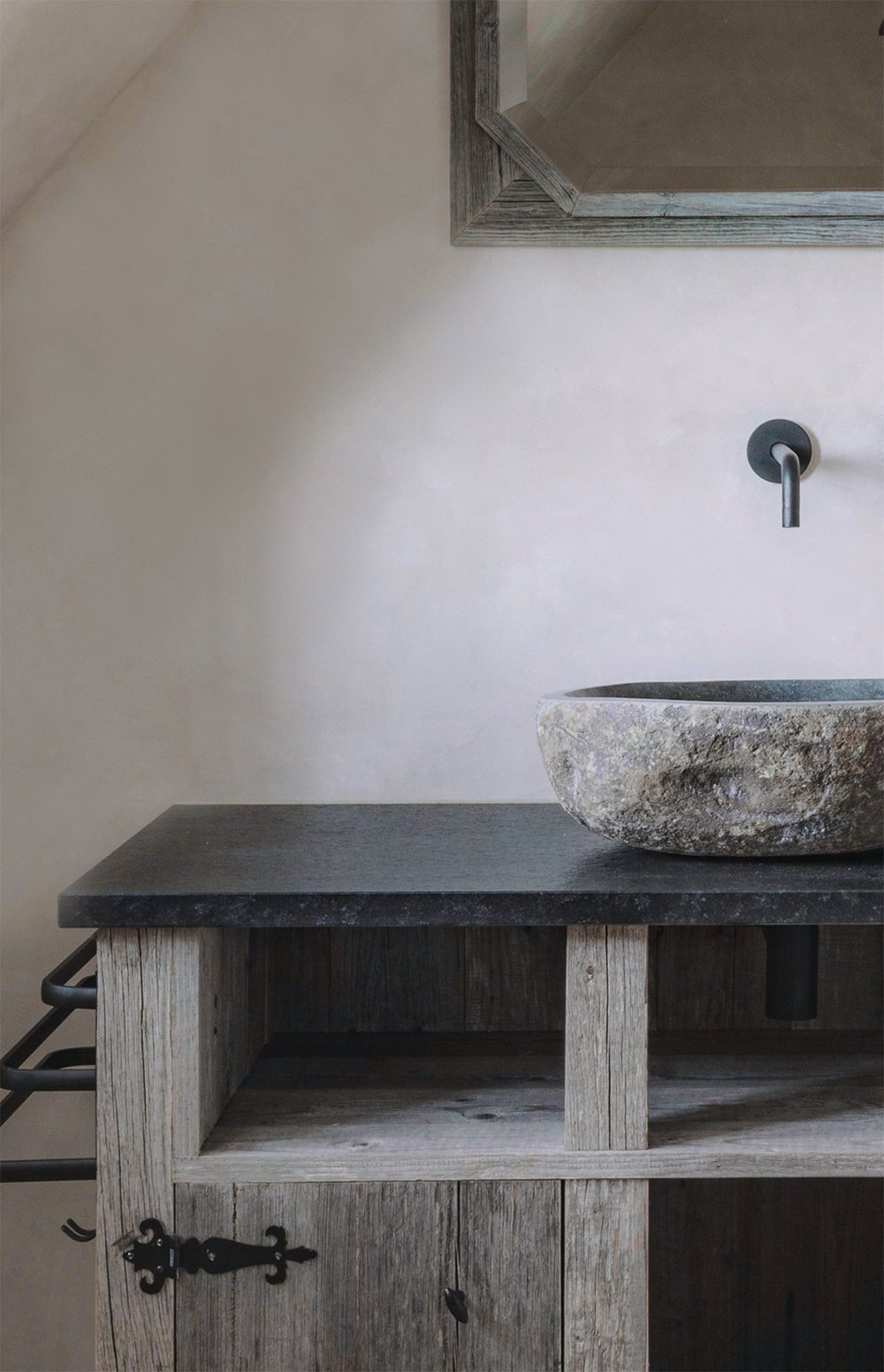 Interieurdetail van een rustieke badkamer met een stenen waskom, houten meubel en wandkraan.