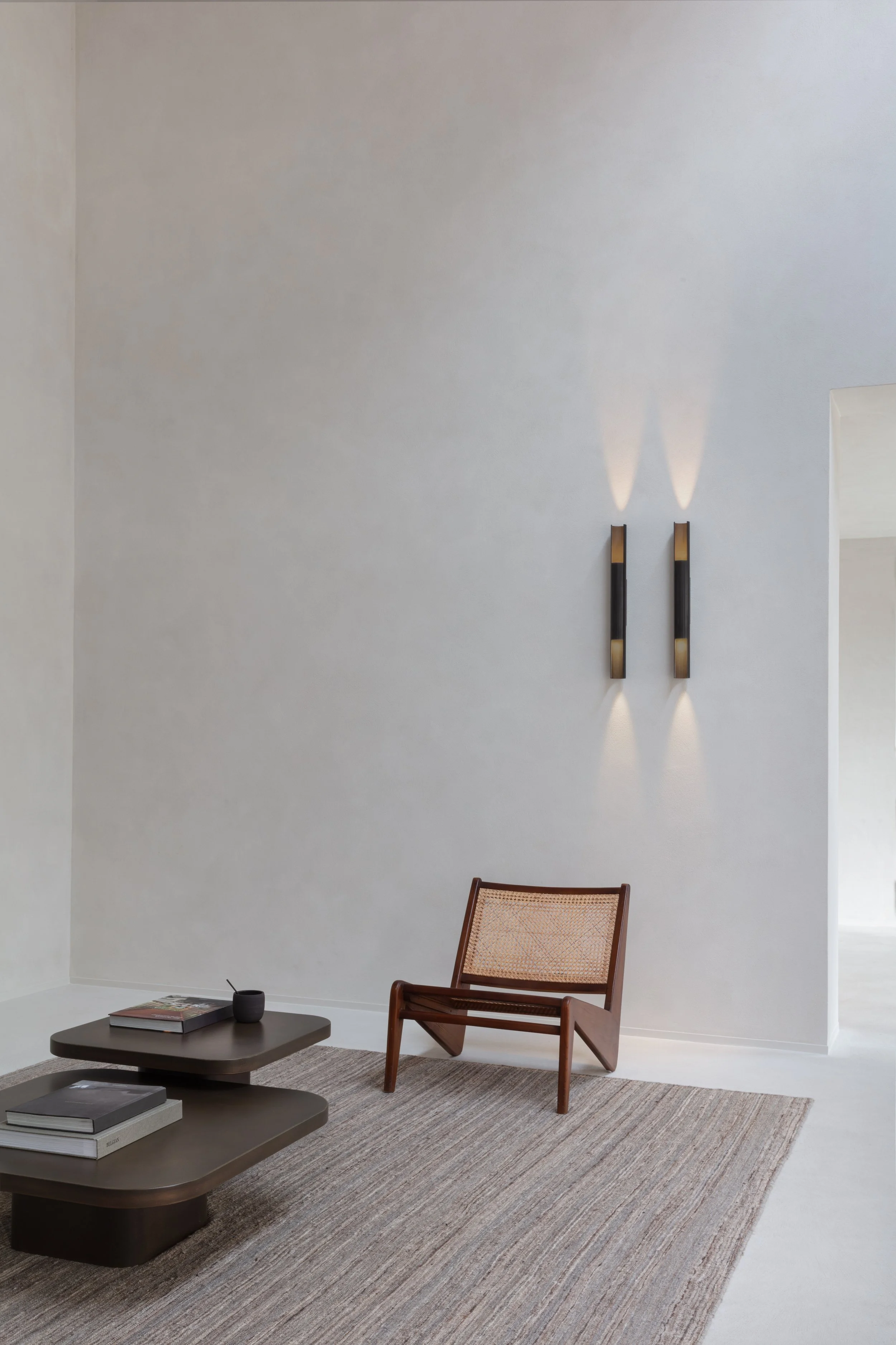Minimalistisch interieur met houten stoel, lage salontafel, gestreept vloerkleed en moderne wandverlichting.