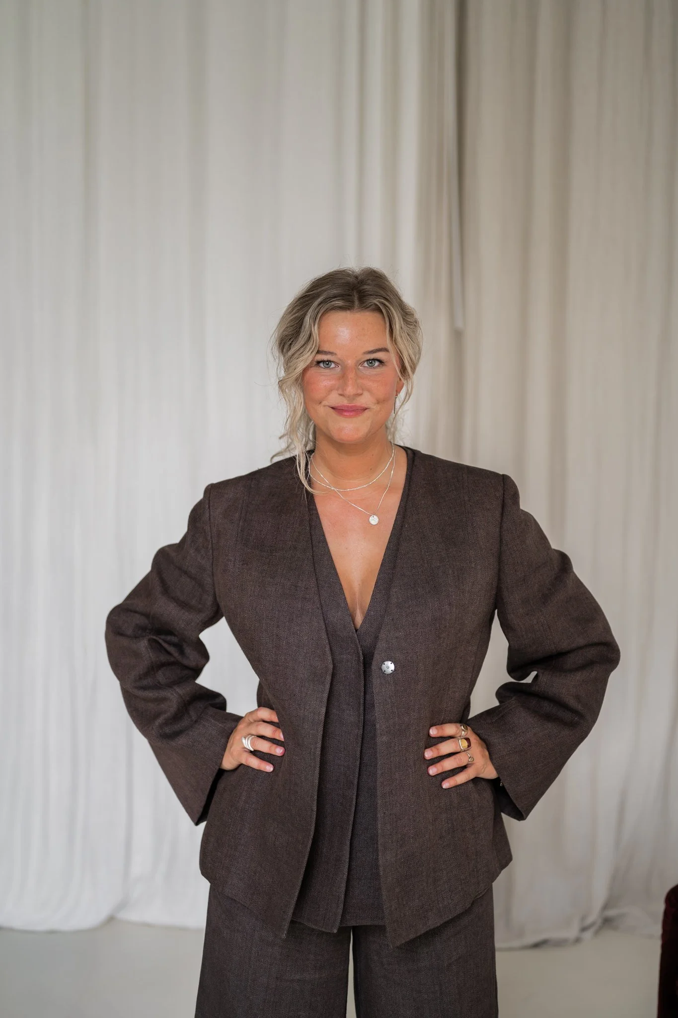 Fotograaf Céline Ronsse van Studio Cé in een bruin pak voor een lichte achtergrond.