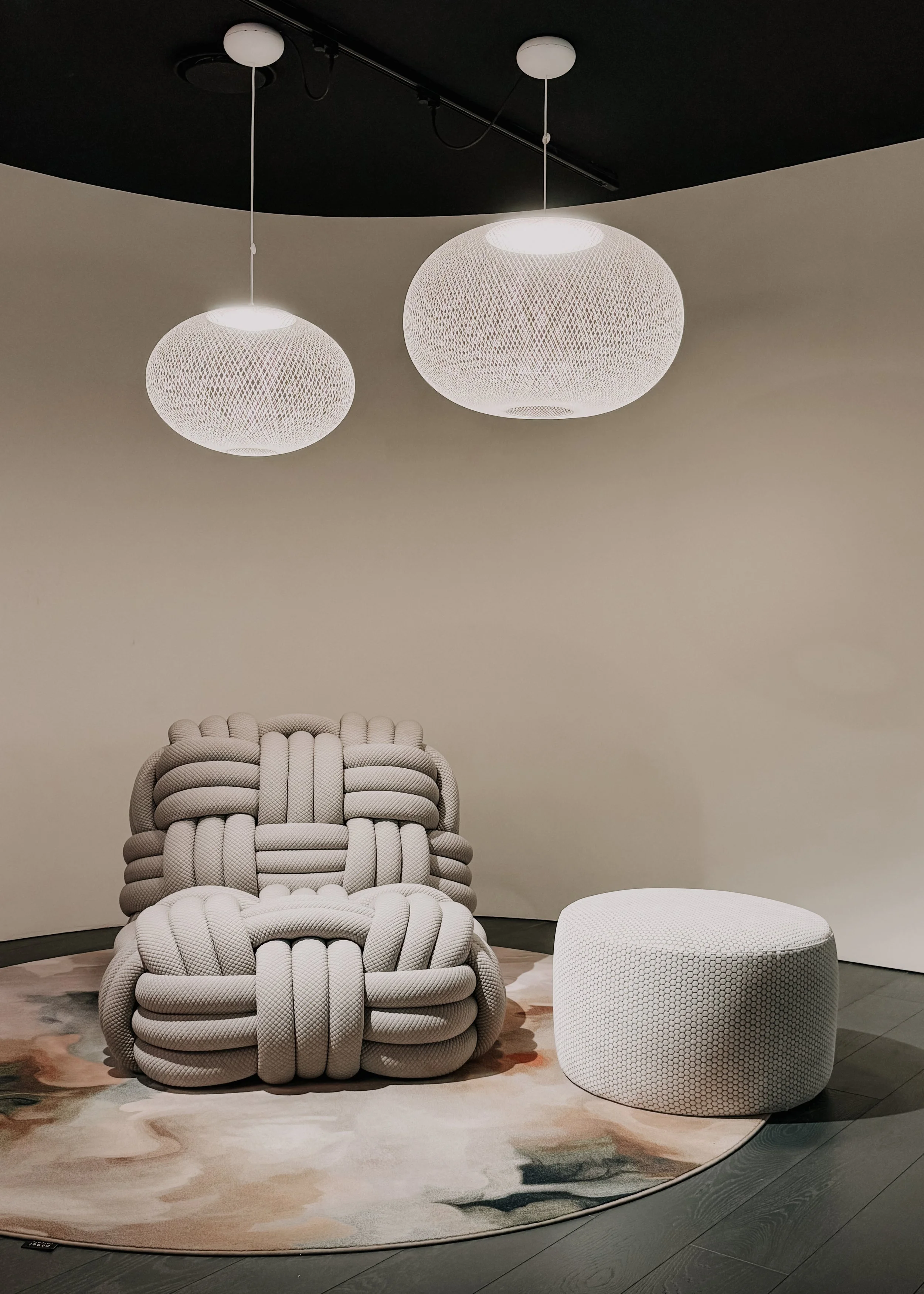 Modern interieur met witte designfauteuil, ronde poef en bolvormige hanglampen.