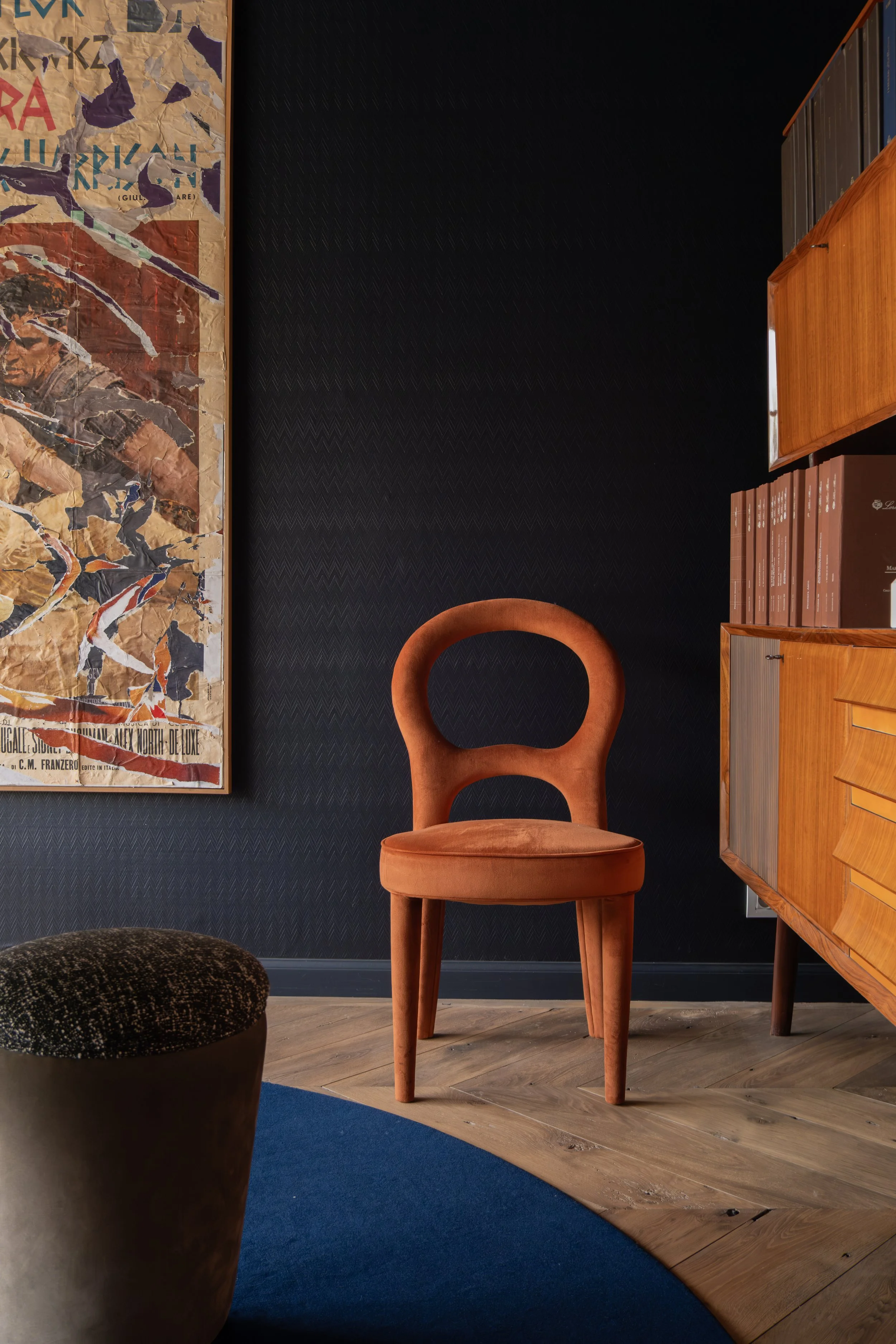 Eclectisch interieur met vintage houten stoel, blauwe wand, boekenkast en kleurrijke wandkunst.