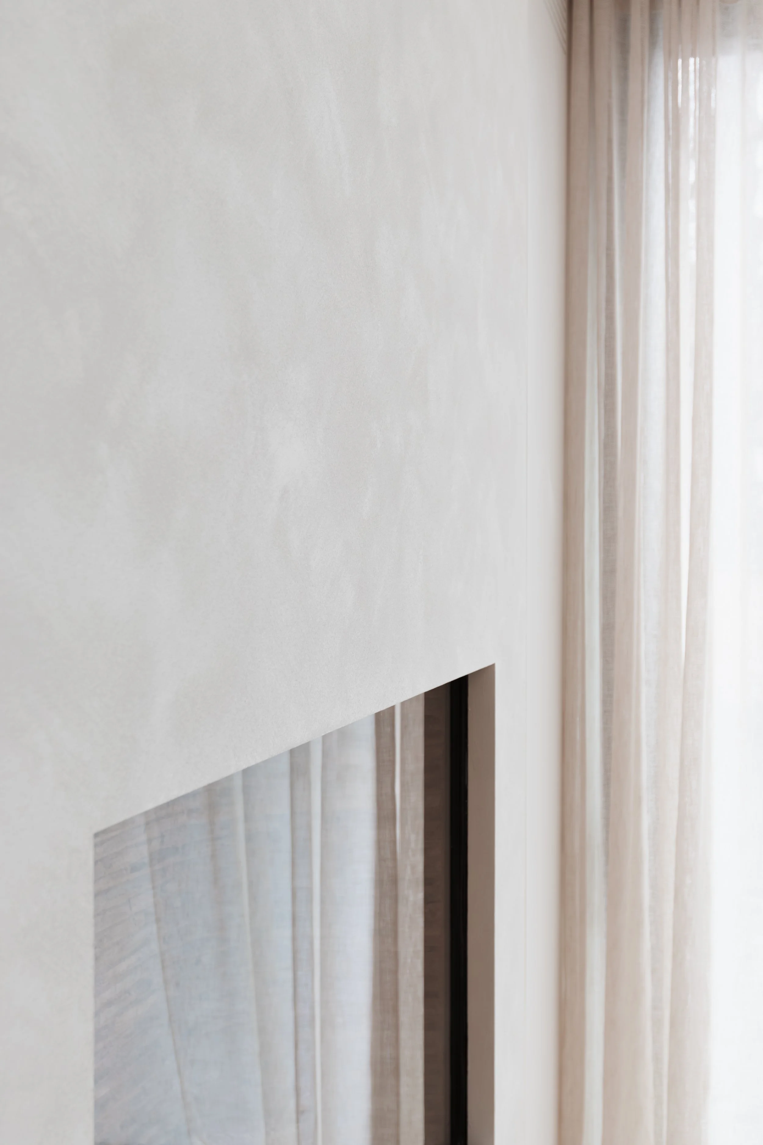 Minimalistisch interieurdetail met een raam, lichte gordijnen en een subtiel afgewerkte wand.