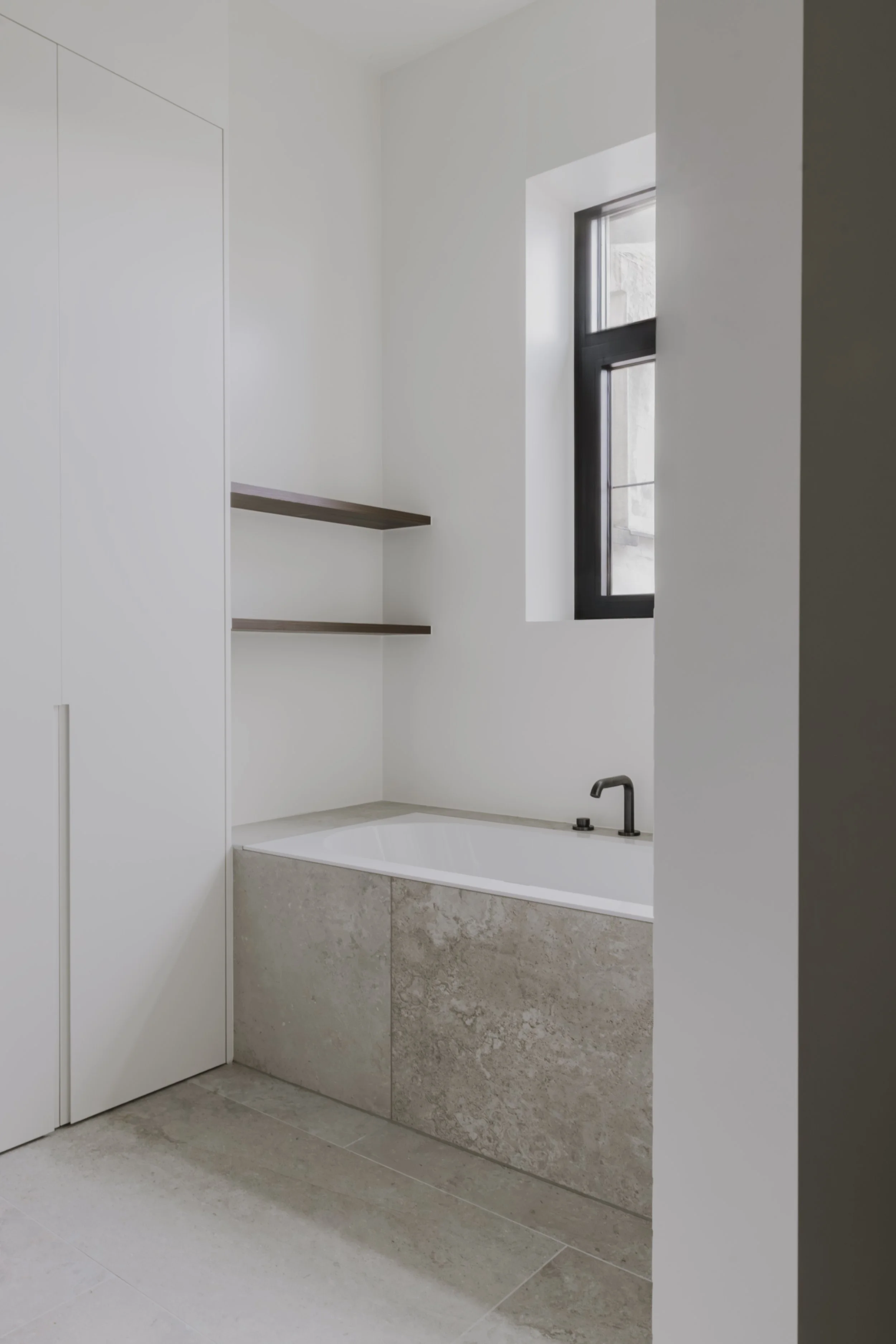 Moderne badkamer met ligbad, beige marmer, lichte tegelvloer en zwart omlijst raam.