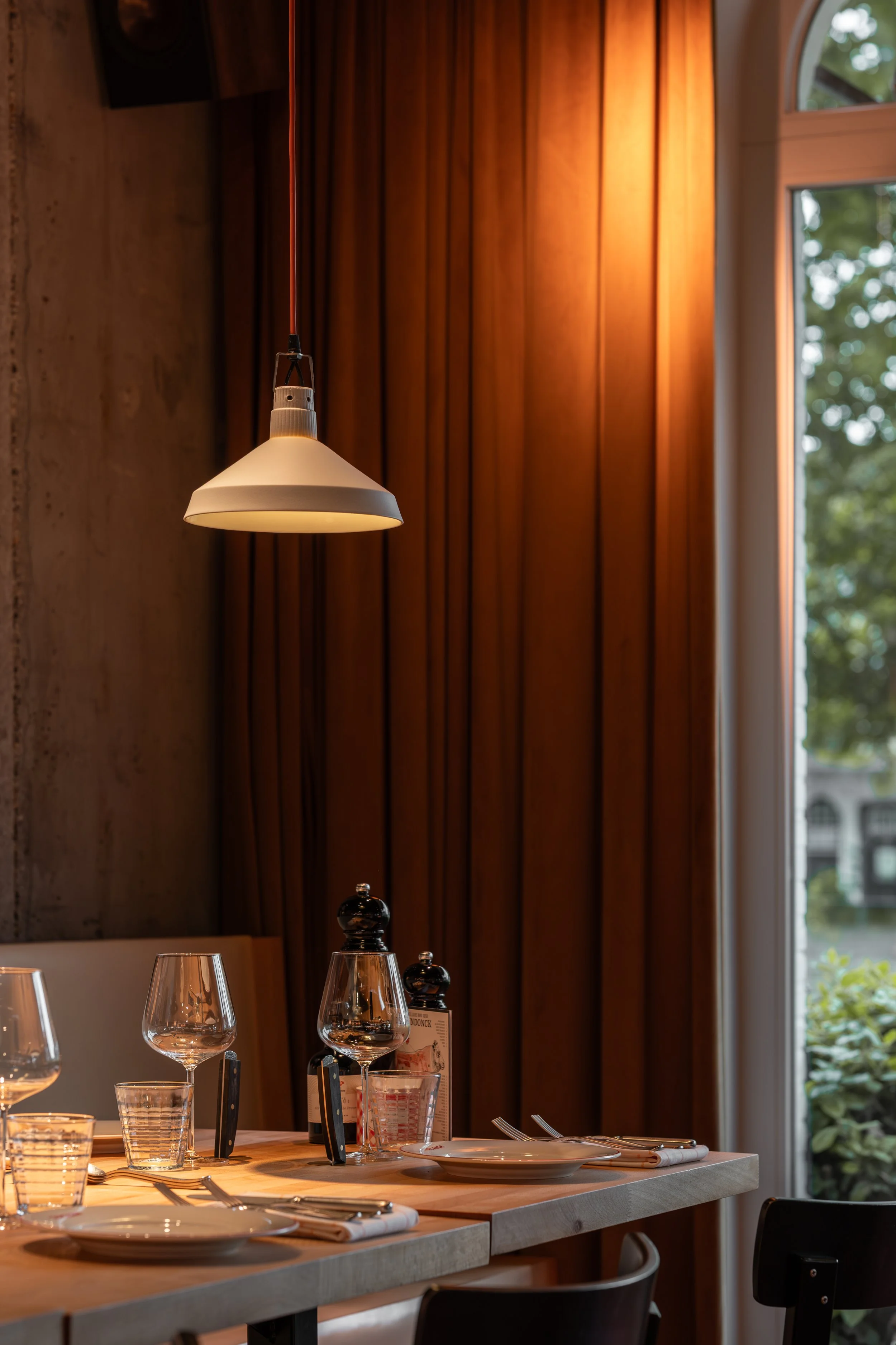 Stijlvol gedekte restauranttafel met wijnglazen en servies, omringd door warme houttinten.