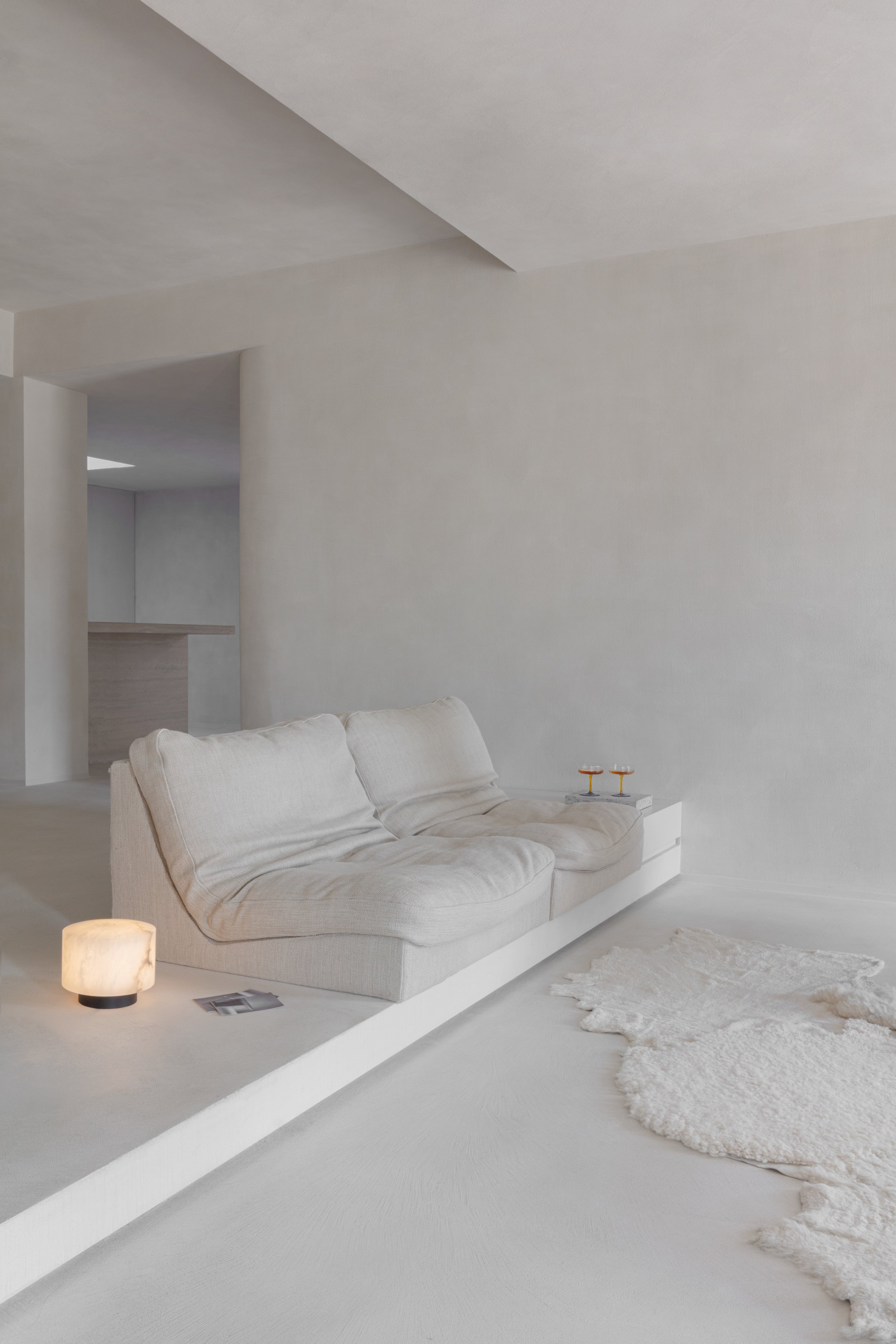 Lichte minimalistische woonkamer met beige zetel, wit vloerkleed en zachte sfeerverlichting.