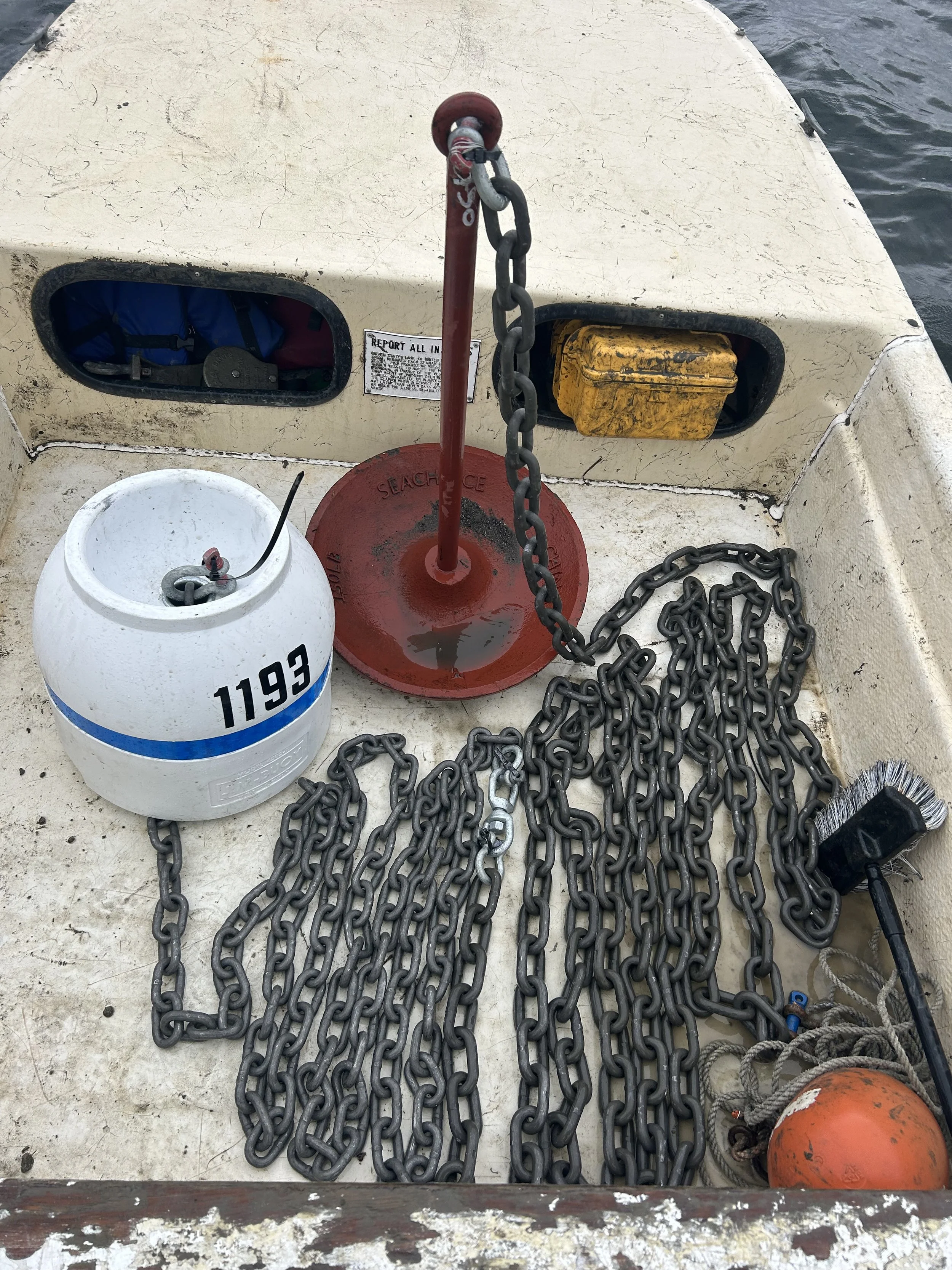 A fishing boat deck with various equipment, including chains, a white container, a yellow box, and an orange buoy.