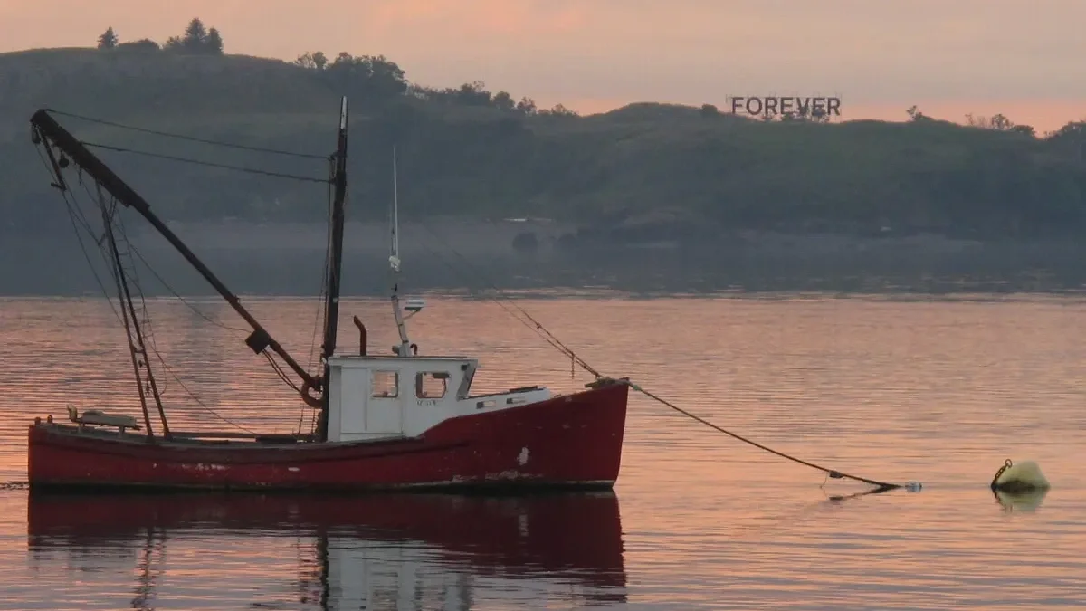 A red boat floating on water at sunset with a hillside in the background.