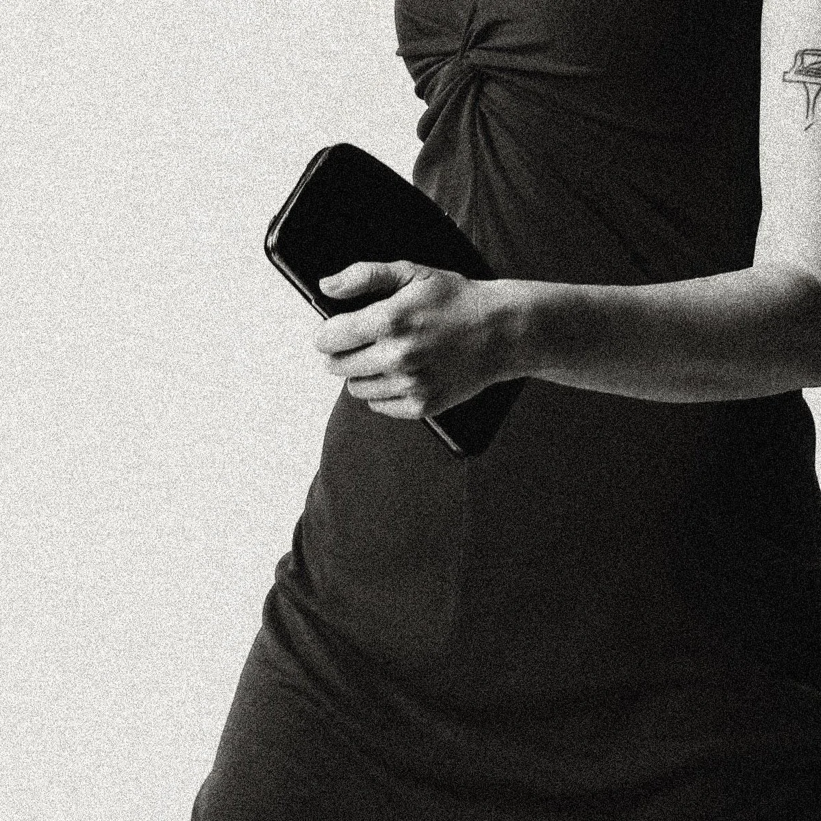 Person holding a smartphone and a notebook in their left hand, wearing a dark dress and walking in motion.