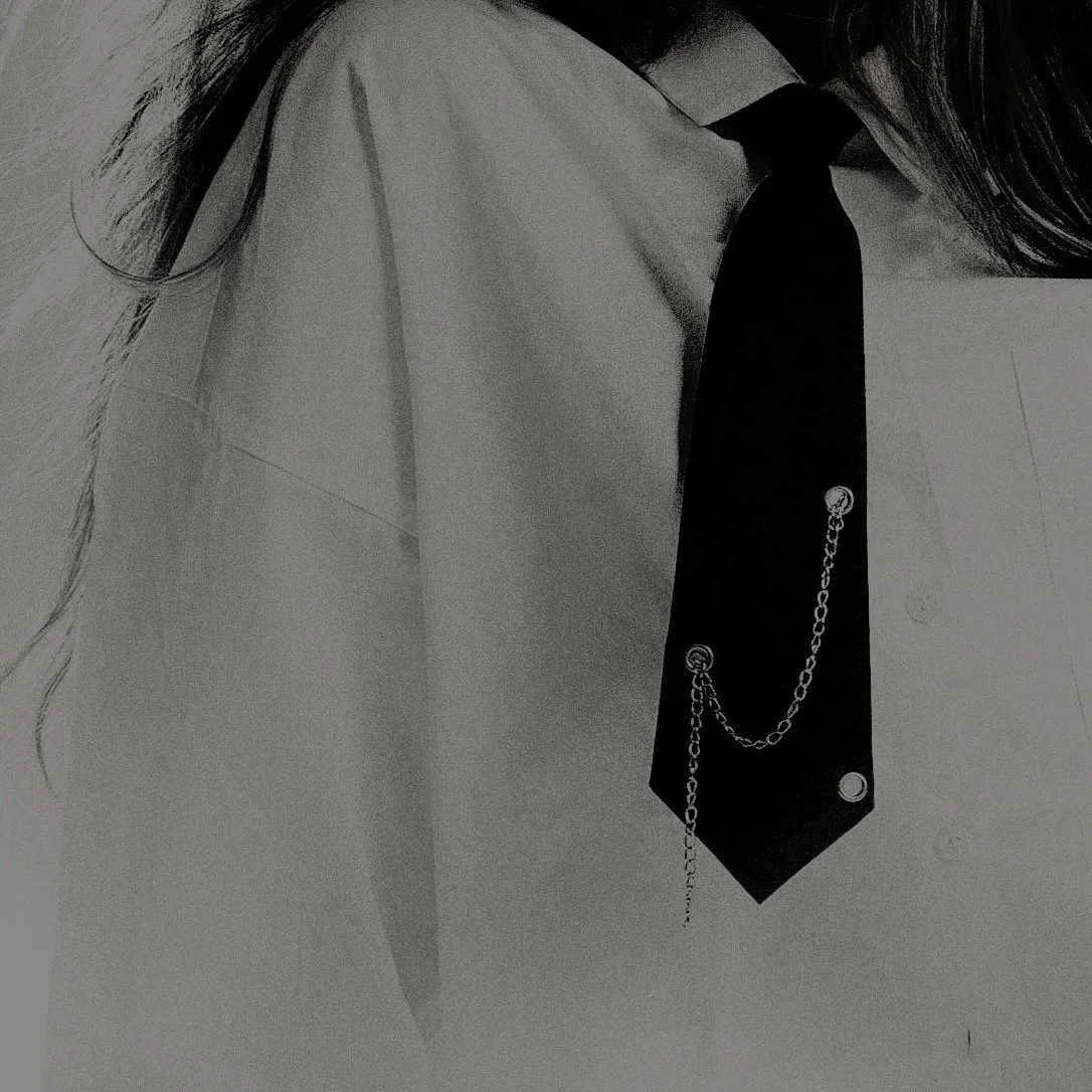 Close-up of a woman wearing a white shirt with a black tie decorated with small metal chains and buttons.