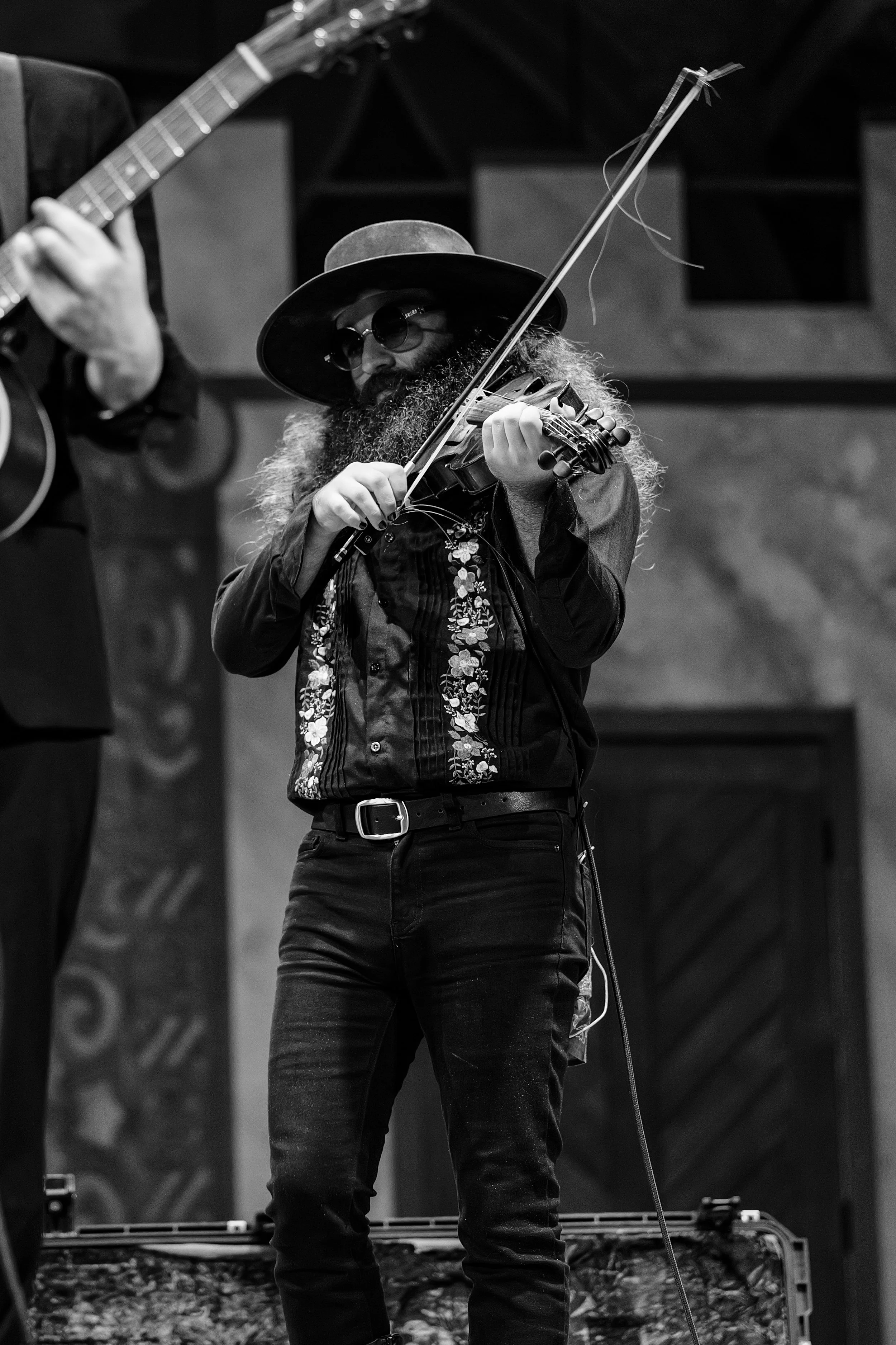 A bearded violinist in a hat and sunglasses performs onstage.