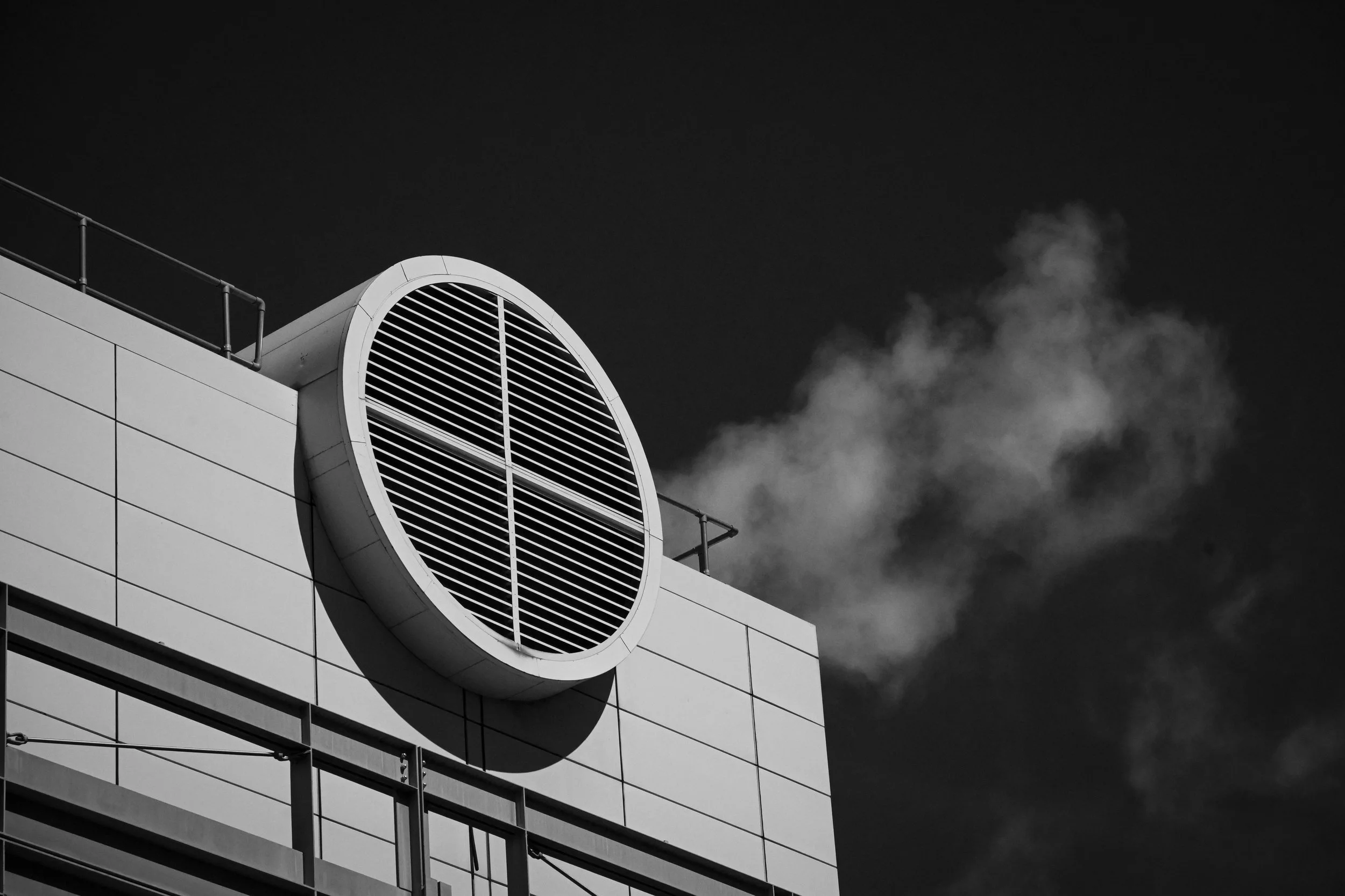 A circular ventilation grille projects from a white building beneath drifting clouds.