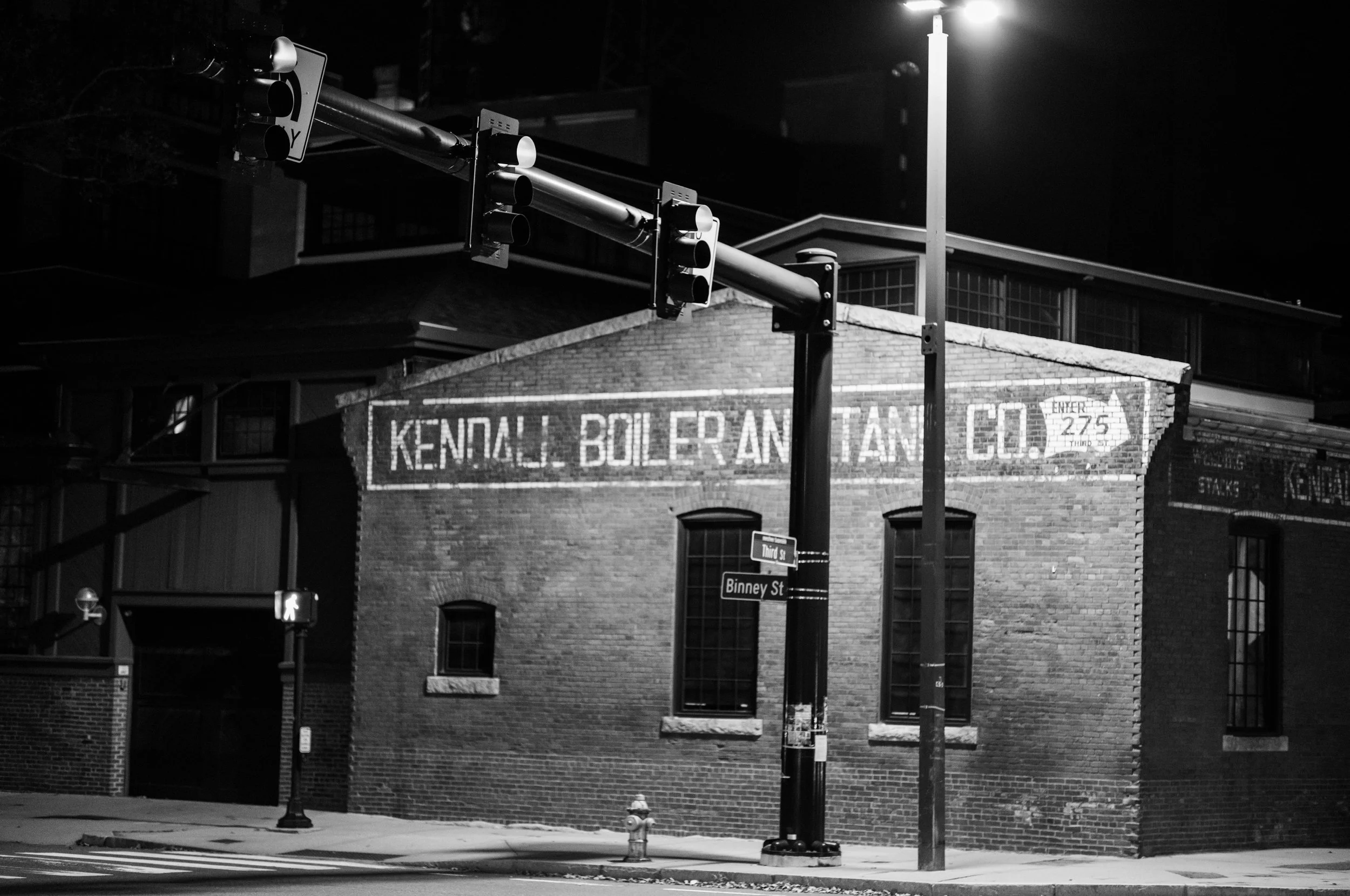 Streetlights illuminate an old brick industrial building on a quiet corner at night.