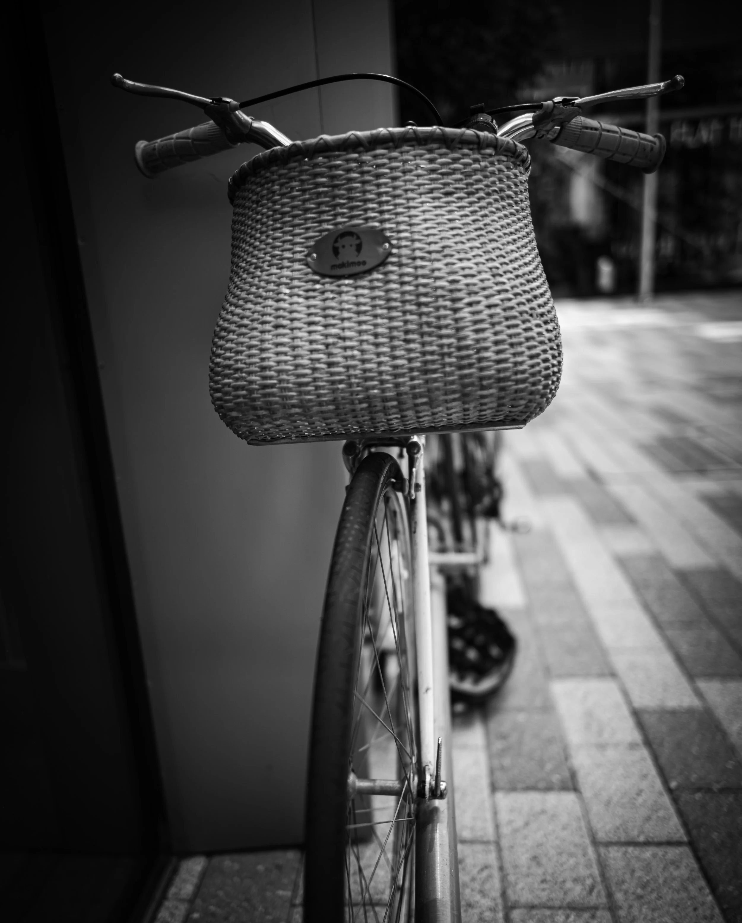 A bicycle with a woven basket rests beside a building.