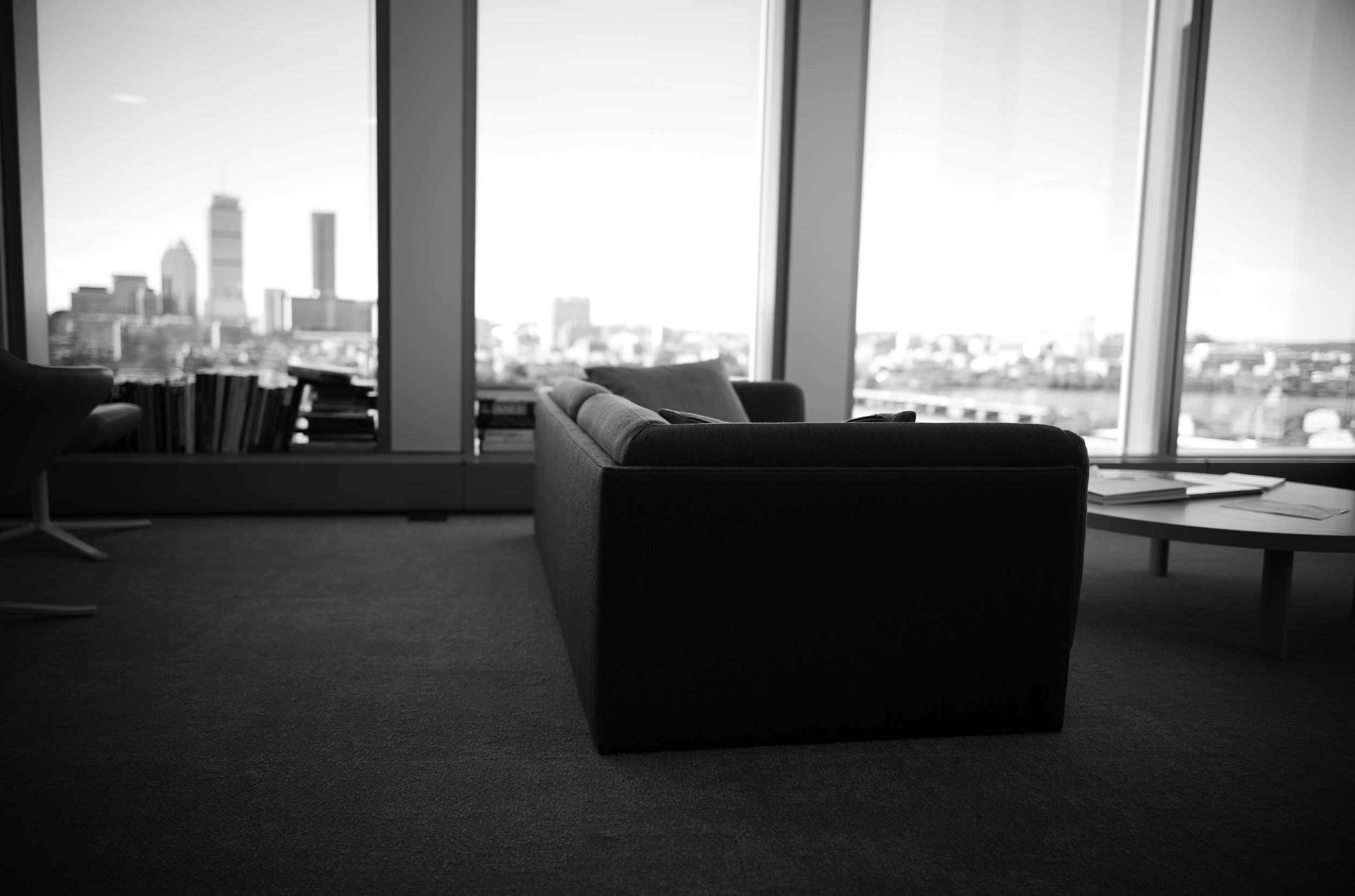 An empty armchair faces tall windows overlooking the city skyline.