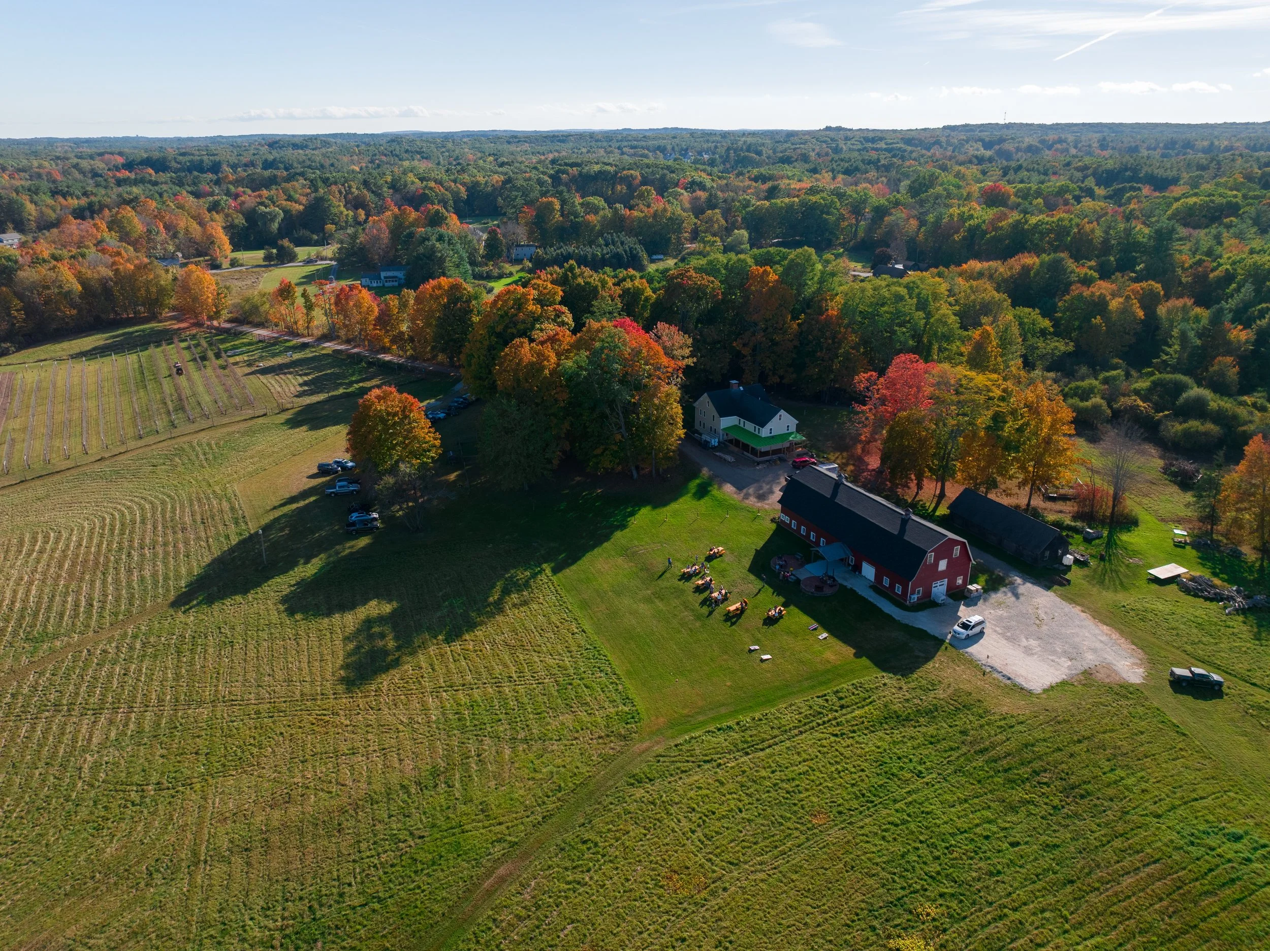 An aerial view of a farm, red barn and fields surrounded by autumn woodland.