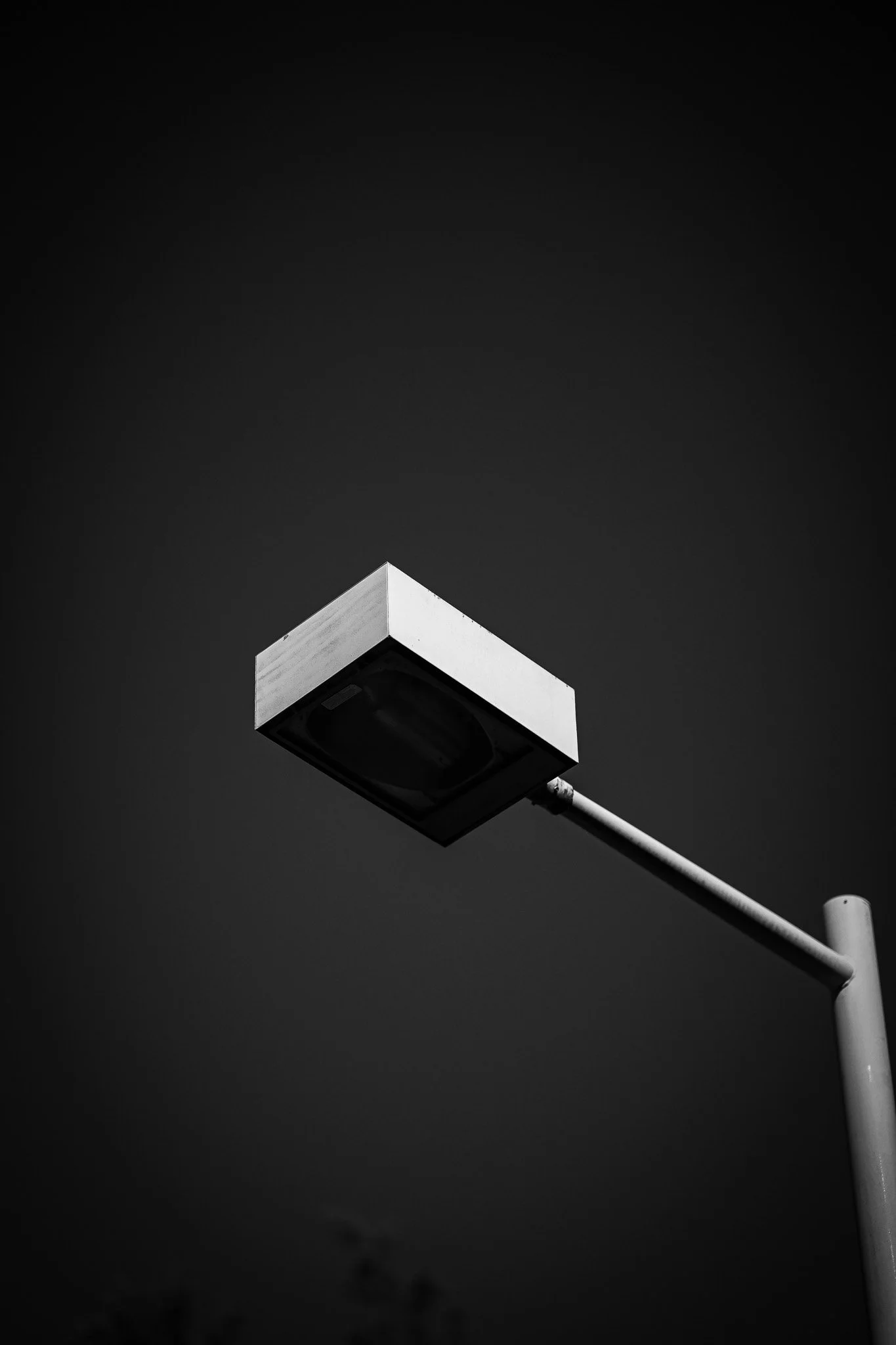 A square streetlight extends diagonally into a dark sky in a minimalist black-and-white photograph.