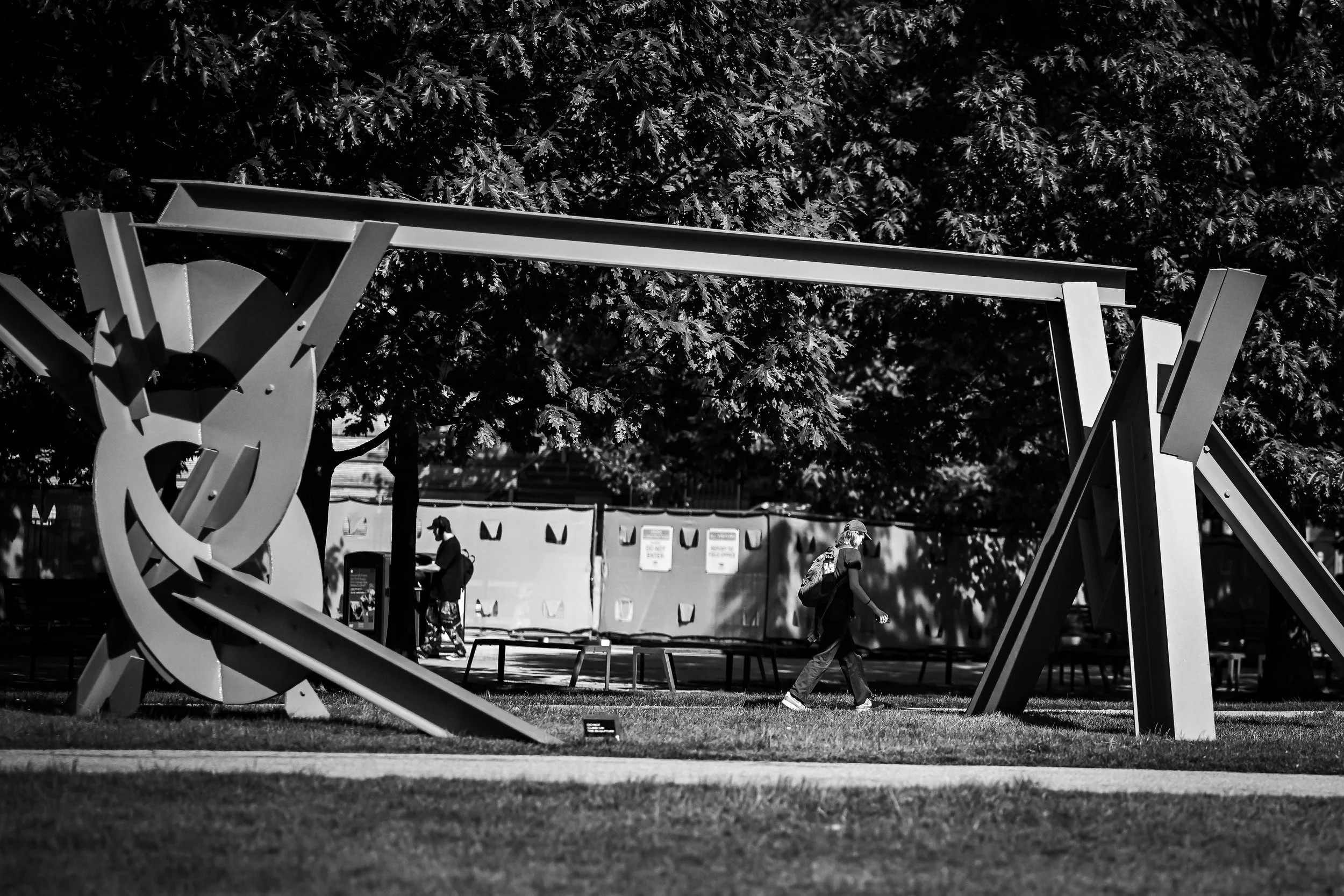 A large abstract outdoor sculpture stands beneath leafy trees.