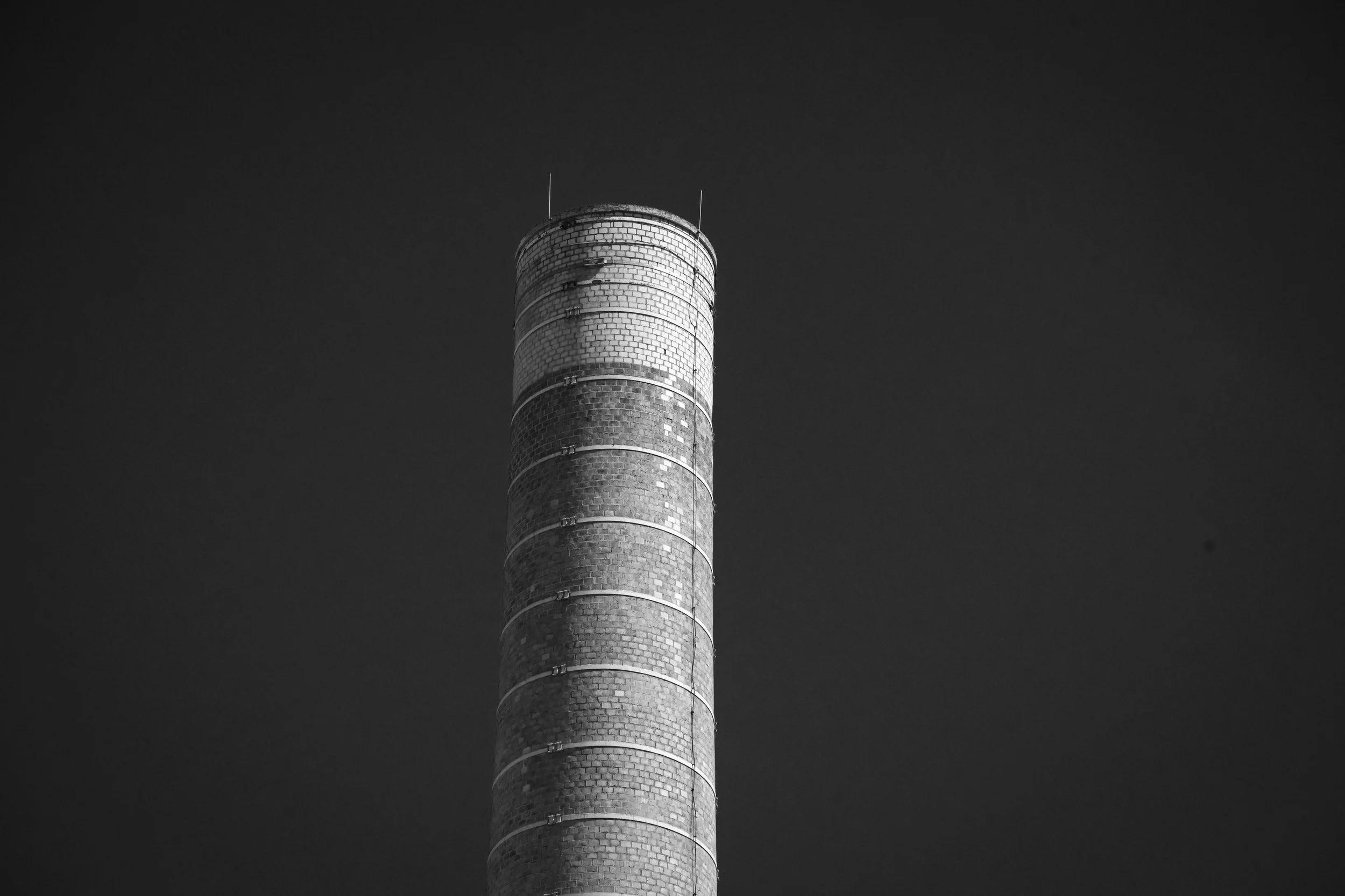 A cylindrical brick chimney rises against a dark, clear sky.