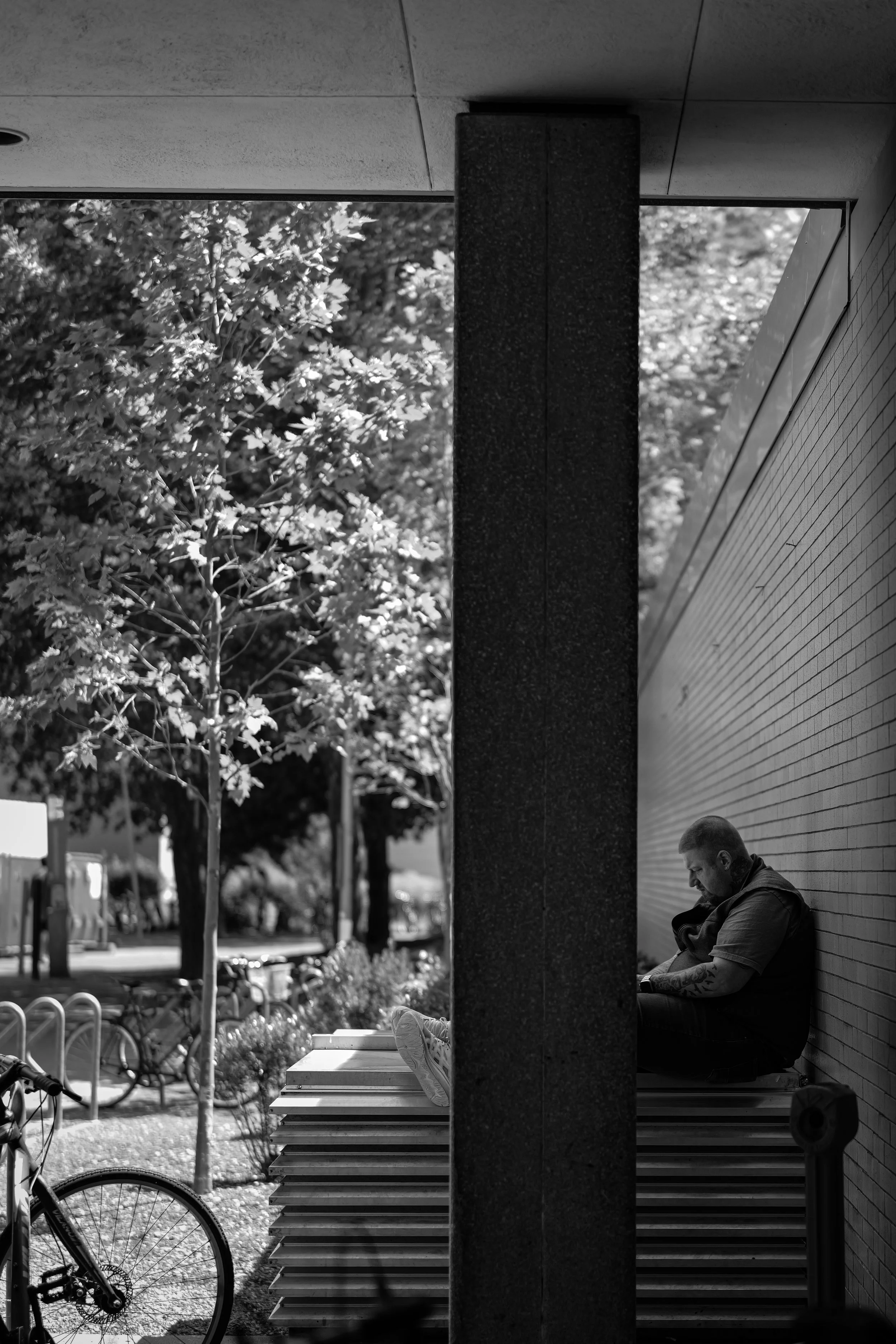 A person rests beside outdoor steps and a tall column beneath trees.