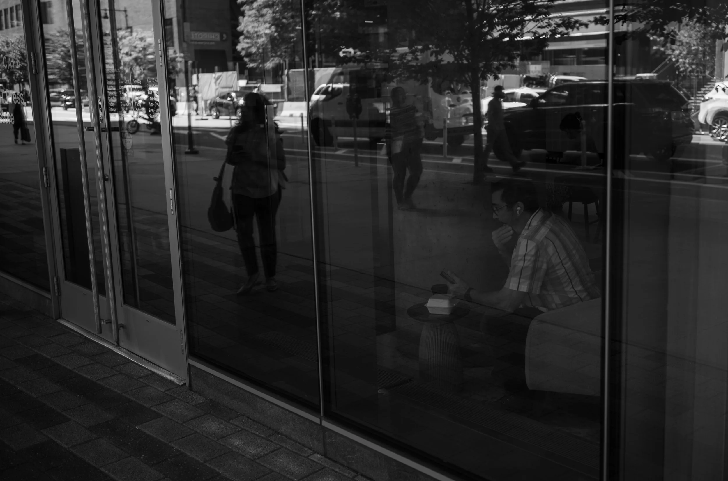 Pedestrians and city buildings reflect in a glass facade.