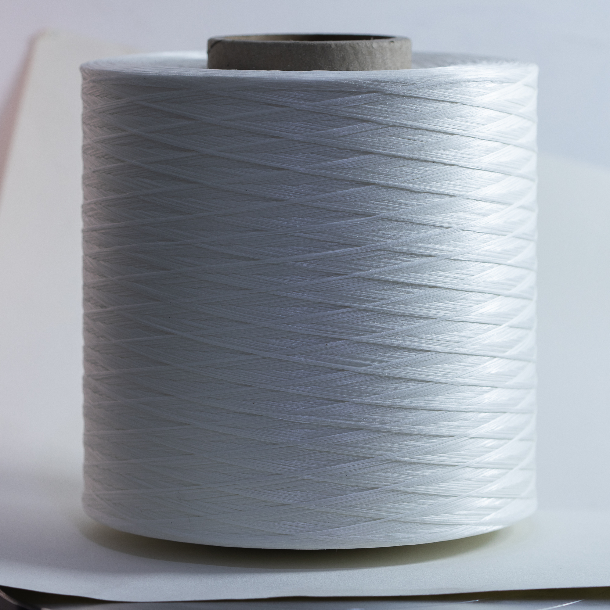 Close-up of a large roll of white string or thread, with a gray cardboard core visible at the top, placed on a white surface.