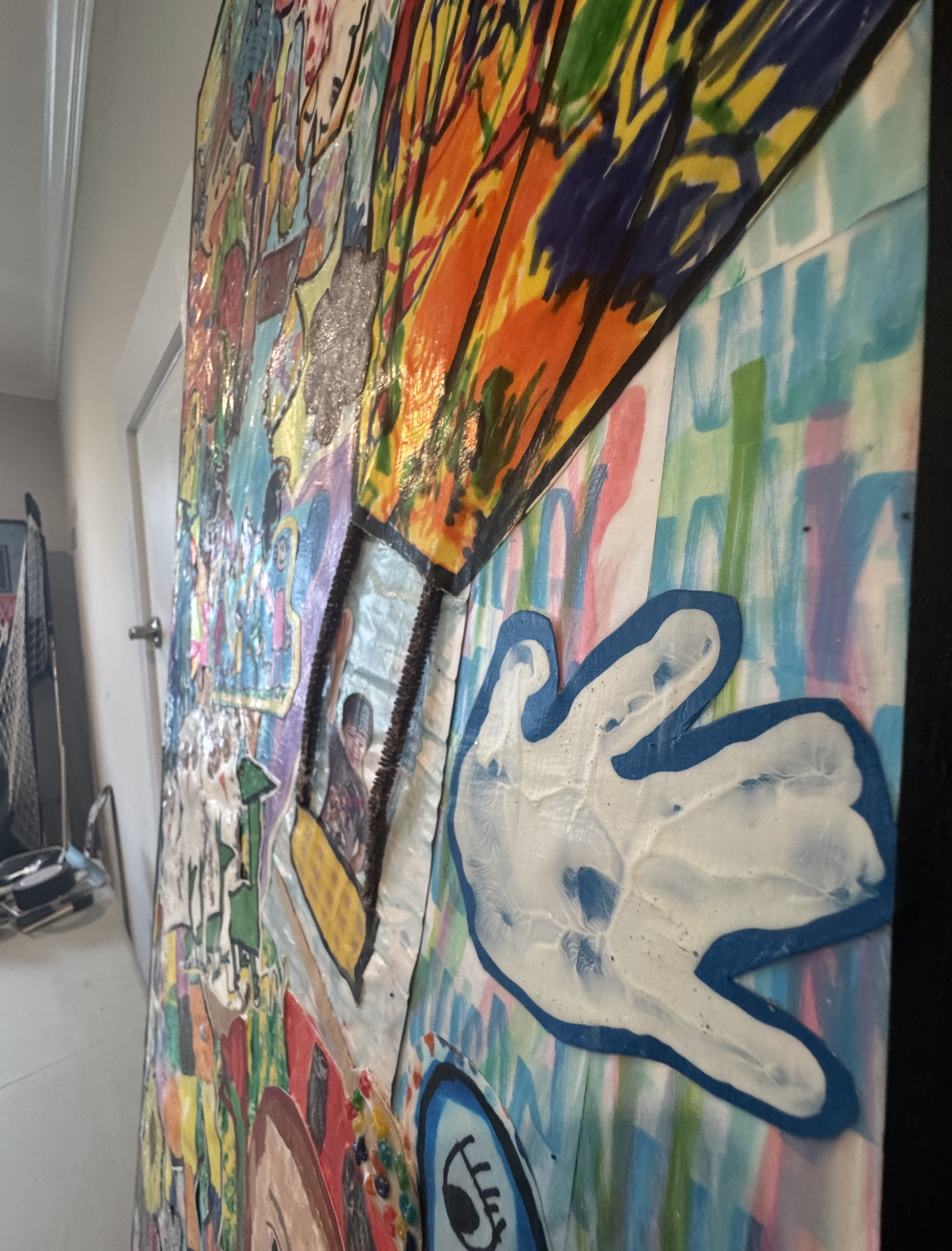Close-up of a large, colorful, and textured collage or mural made of various painted and textured paper, with abstract shapes and vibrant colors.