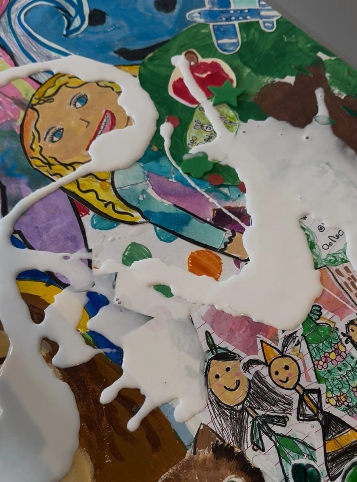 A colorful children's artwork featuring a princess with blond hair and a pink dress, a Christmas tree decorated with star and ornaments, a snowman, and two smiling children holding a Christmas tree, all drawn with markers and cut out paper elements.