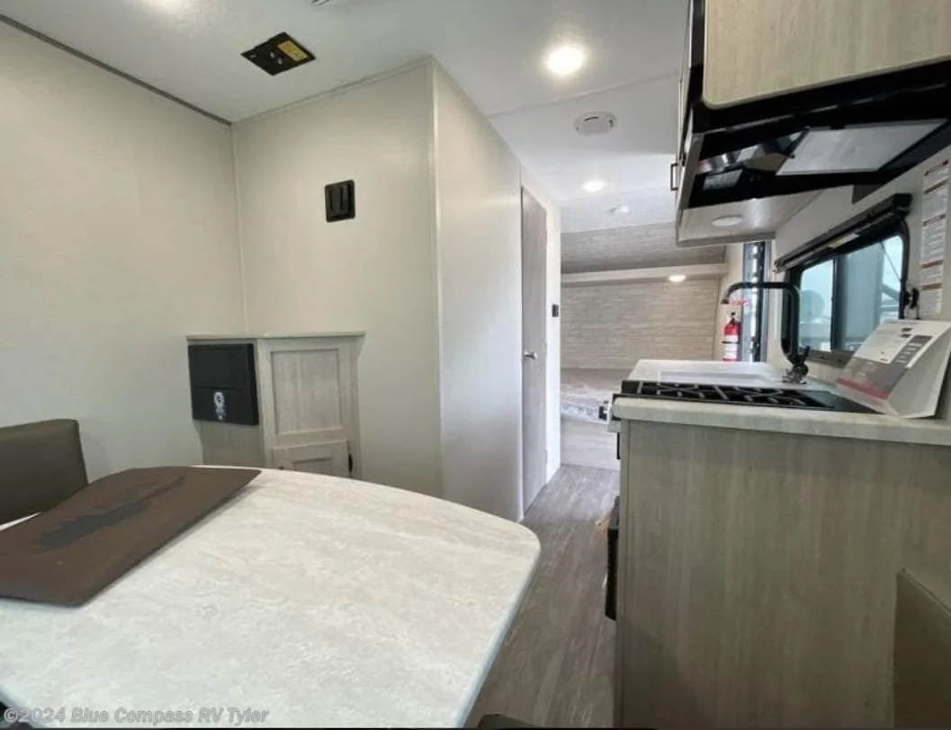 Interior of a small RV with a dining table, kitchen appliances, a window, and a door leading to another space.